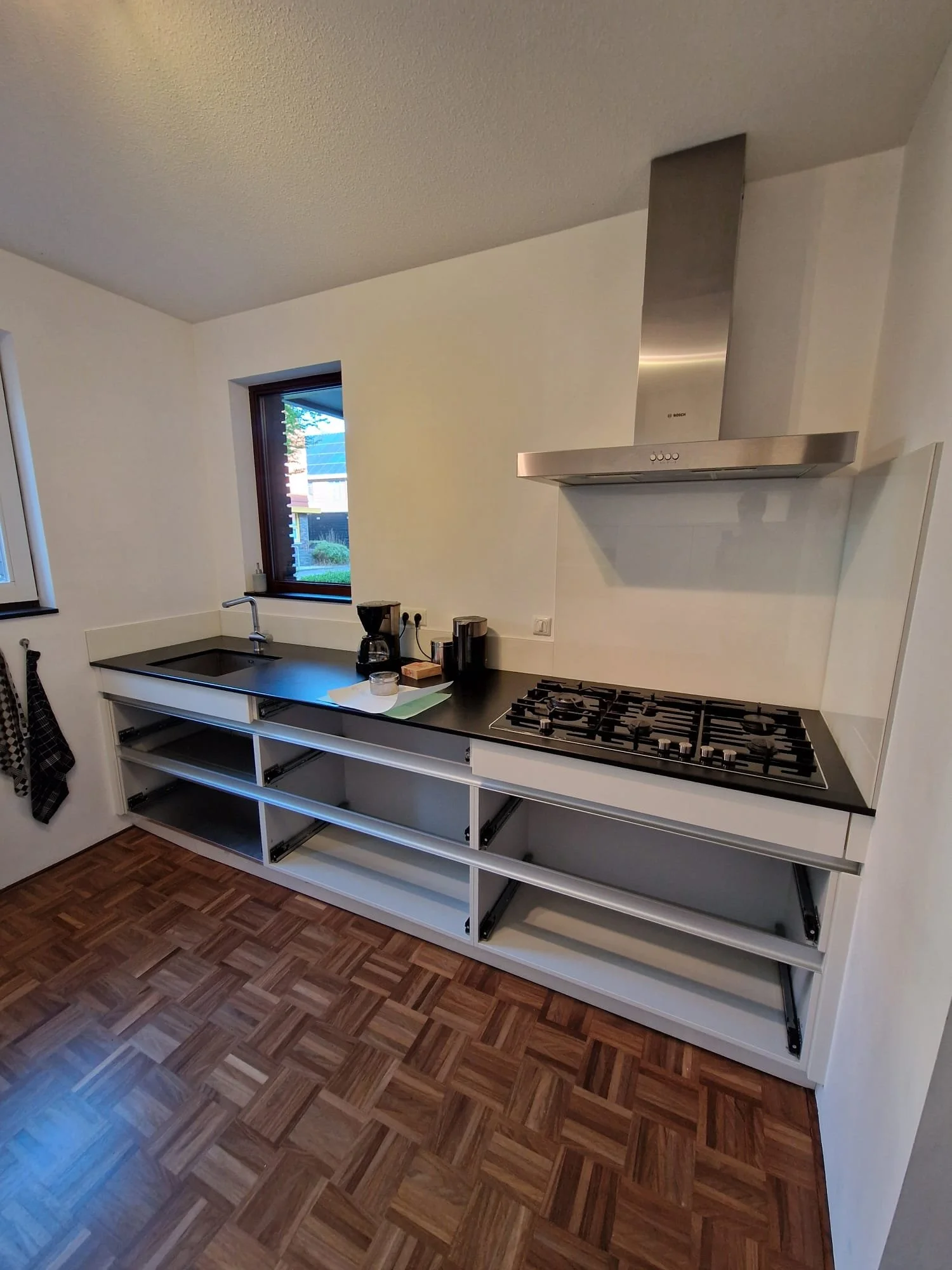 Onvoltooide keuken met lege witte kasten, een zwarte werkblad en een gasfornuis.