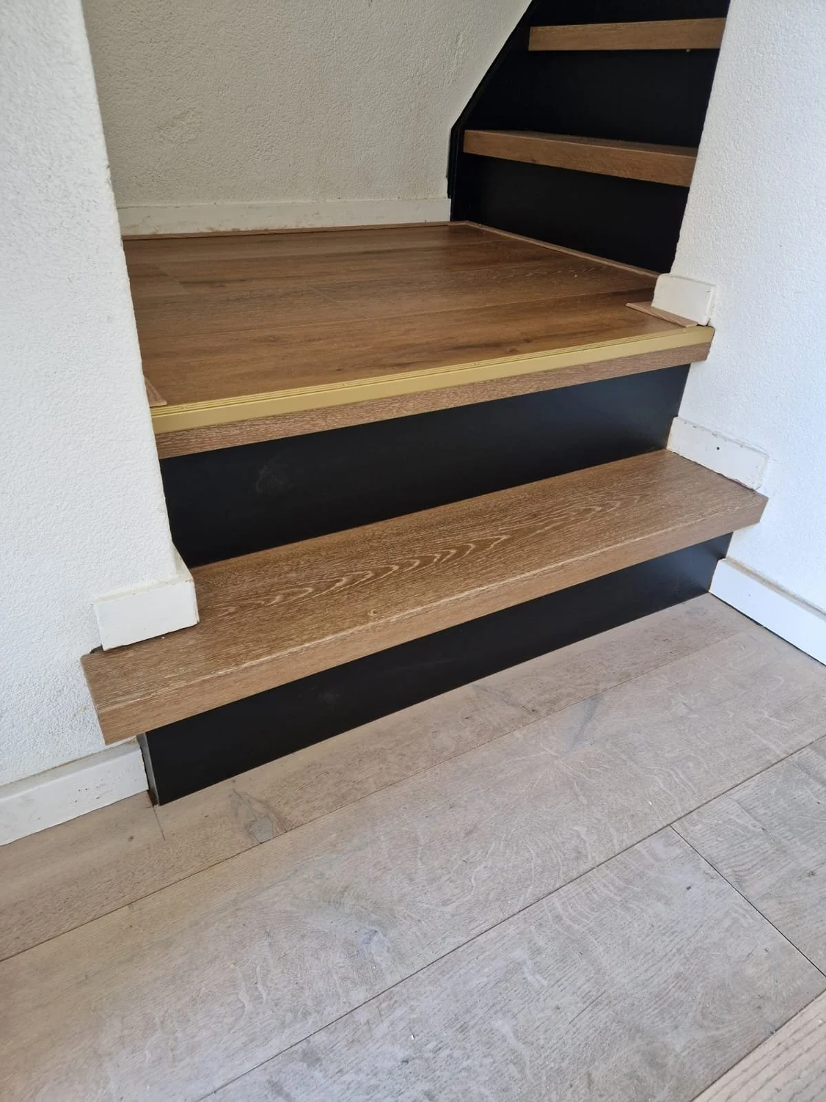 Twee eenvoudige houten trappen met zwarte zijkanten en witte muur en houten vloer eronder.