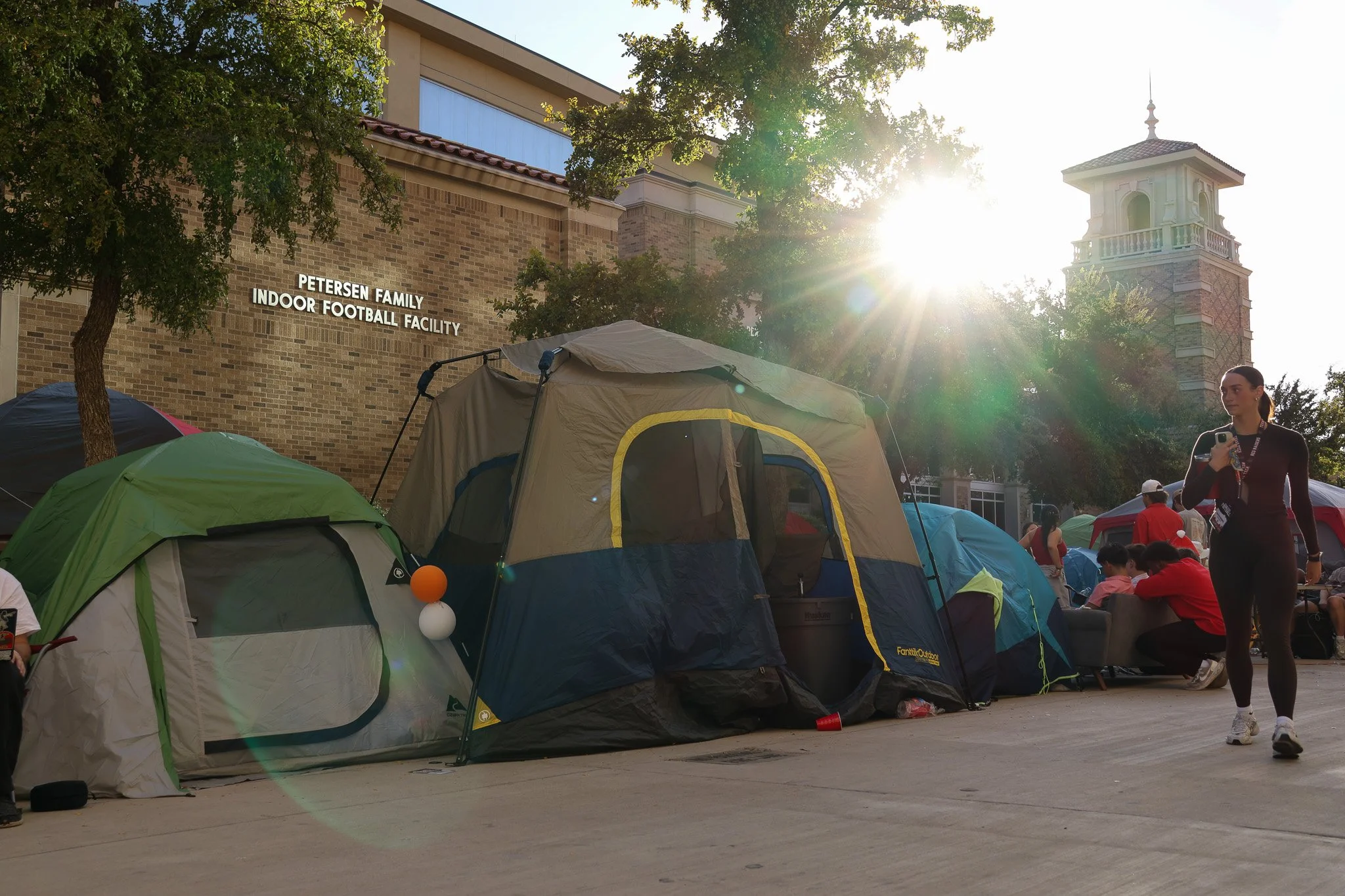 A Texas Tech student walks past other students camping between TTU Athletics' Sports Performance Center and the Jones AT&T Stadium on Nov. 5, 2025 in Lubbock, Texas. The area where the students are camping out is affectionately known as Raiderville.