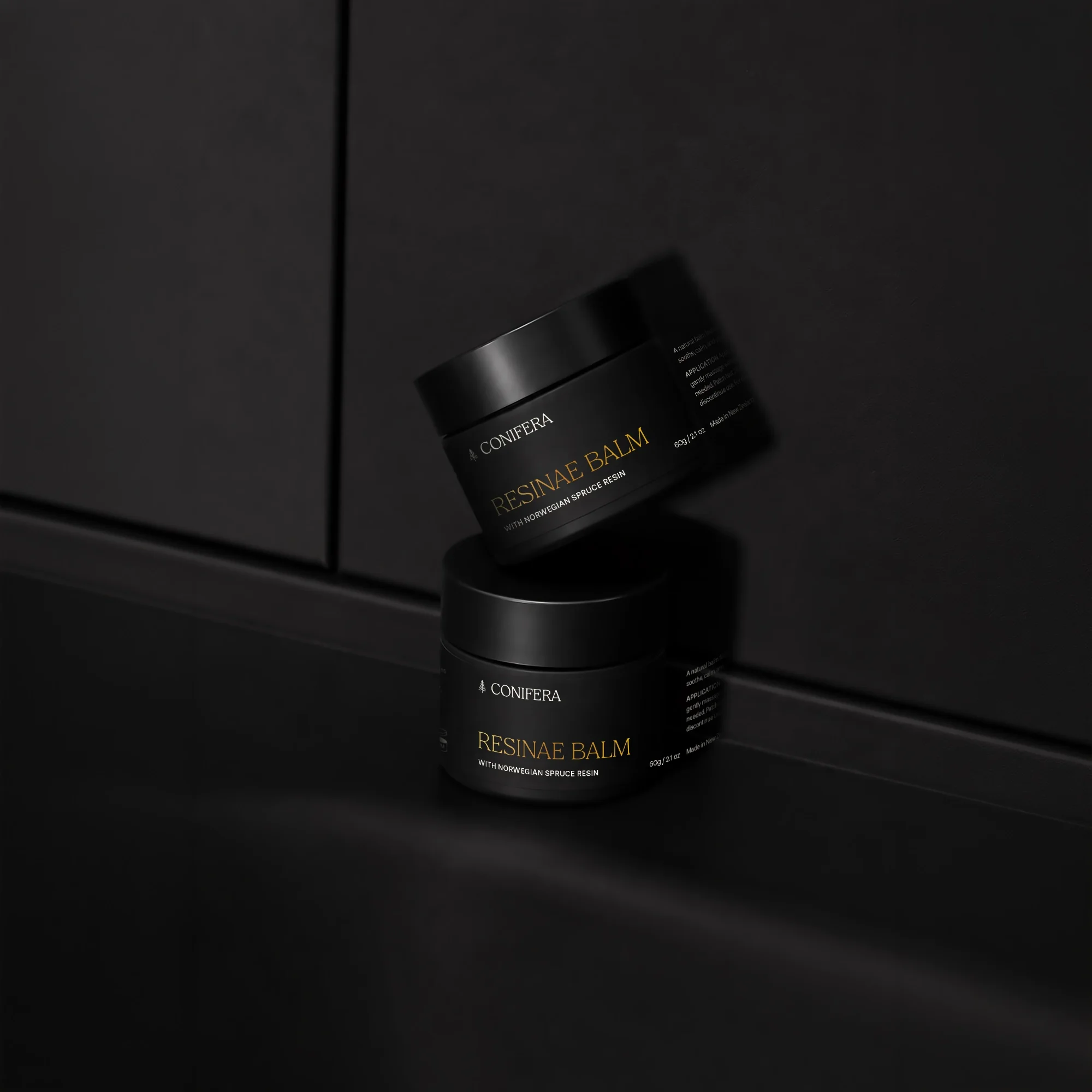 A black container of Resinae Balm with Norweigian spruce resin on a black surface, with a reflection visible.