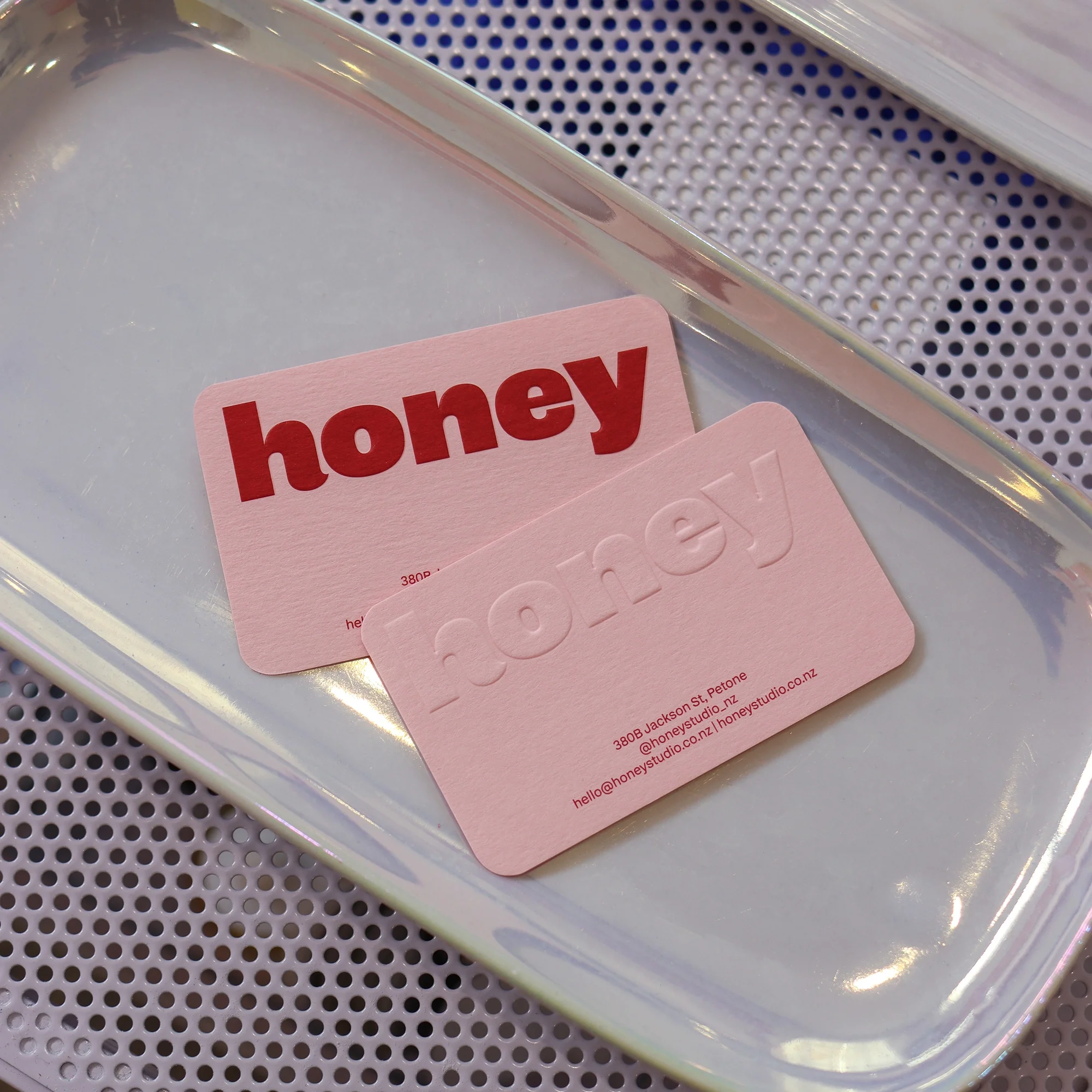 Two Honey business cards on an iridescent tray, one with a red printed logo and one with an embossed logo, showing the Petone, New Zealand address.