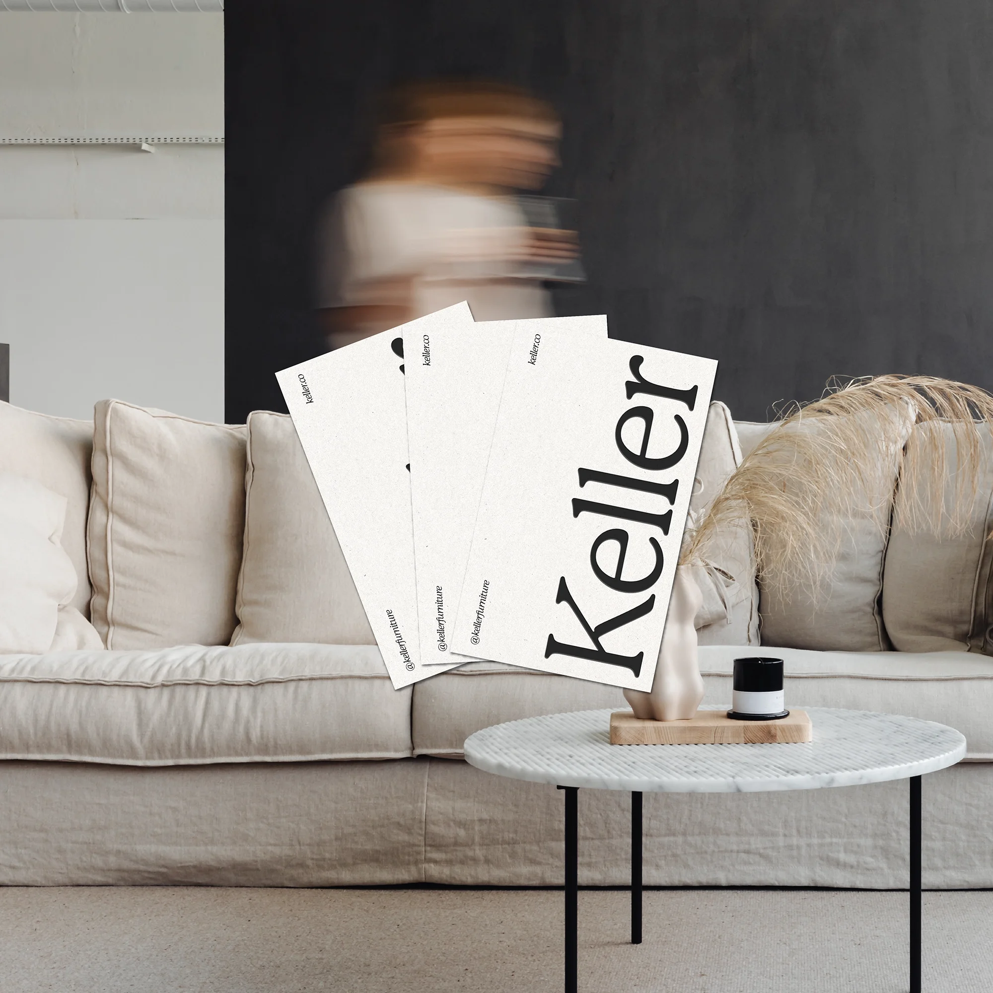 Keller furniture branding business cards with bold serif logo, fanned out on a beige coffee table in a minimalist living room.