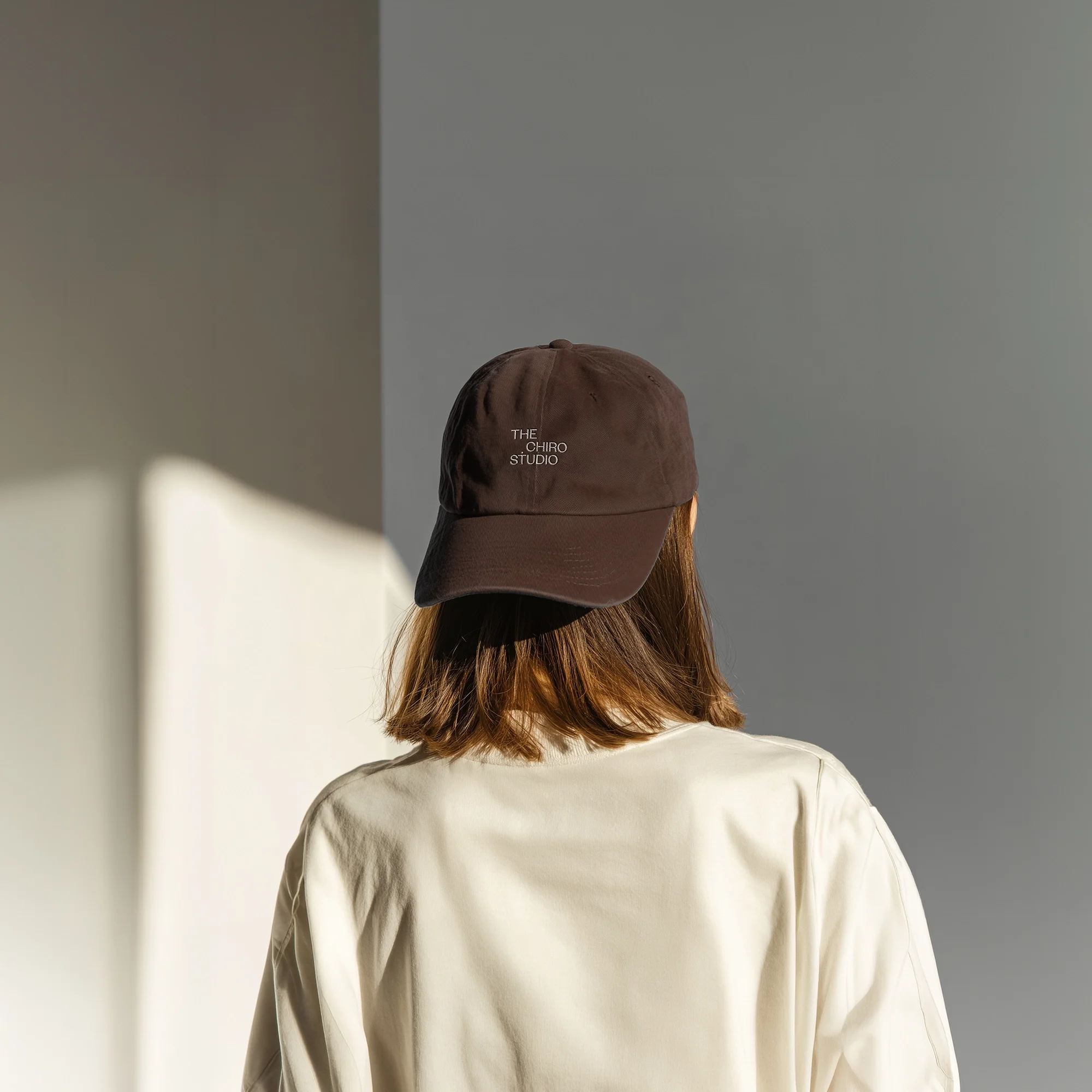 Woman wearing a brown embroidered cap with 'The Chiro Studio' logo, styled against a neutral wall with natural light.