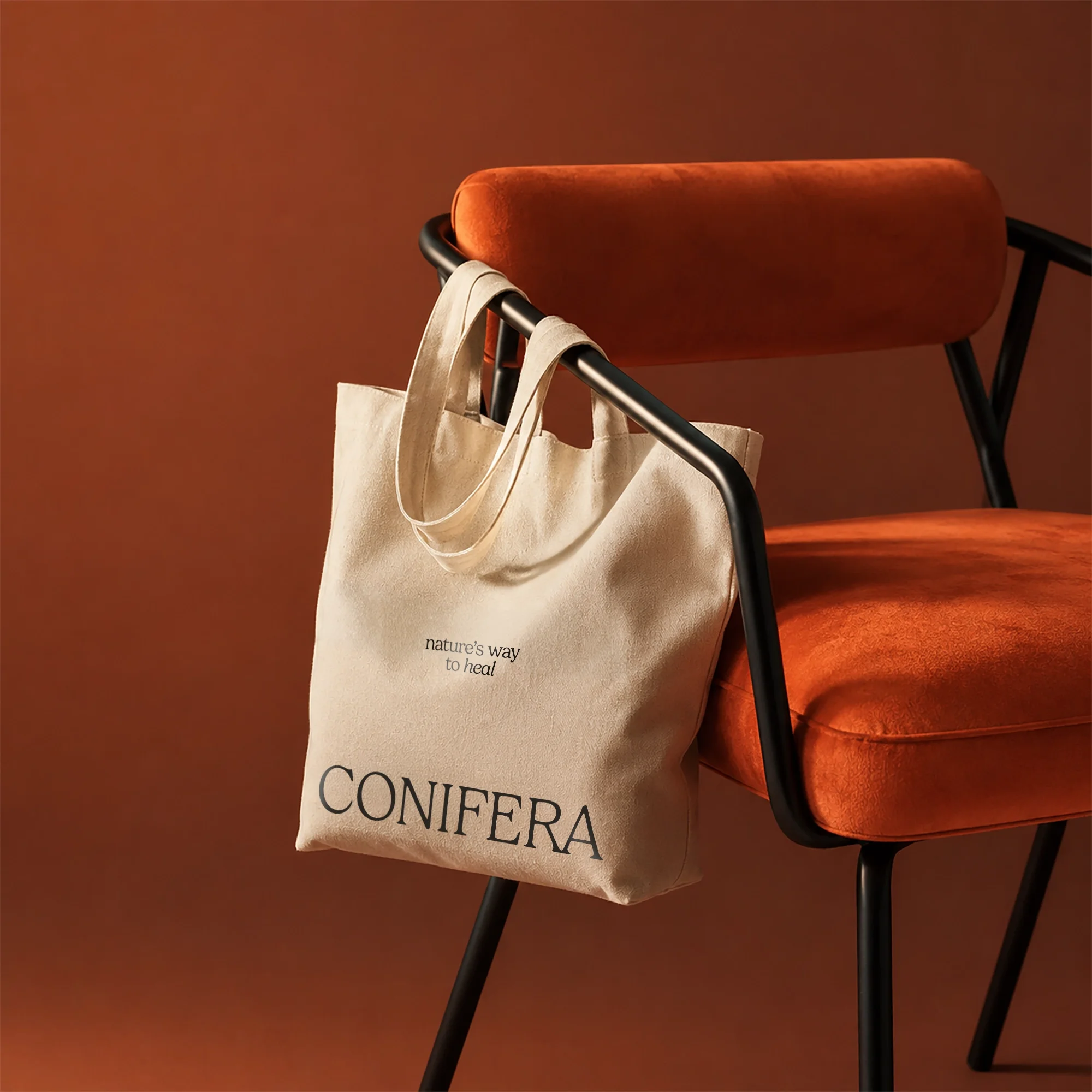 Cream canvas Conifera tote bag with the tagline 'nature's way to heal,' hanging from a burnt orange velvet chair.