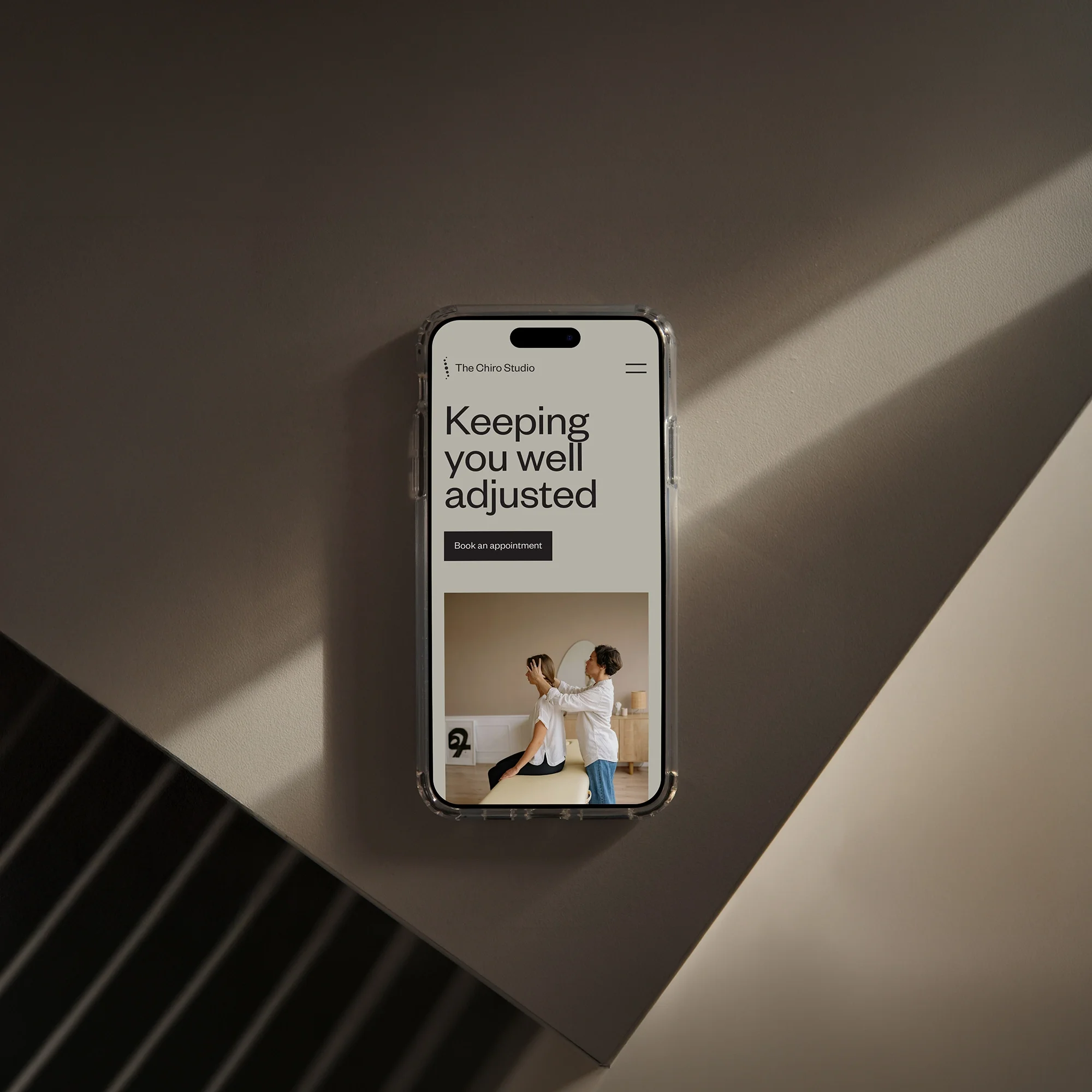 The Chiro Studio website homepage displayed on a smartphone, showing the tagline 'Keeping you well adjusted' above a photo of a chiropractic adjustment.