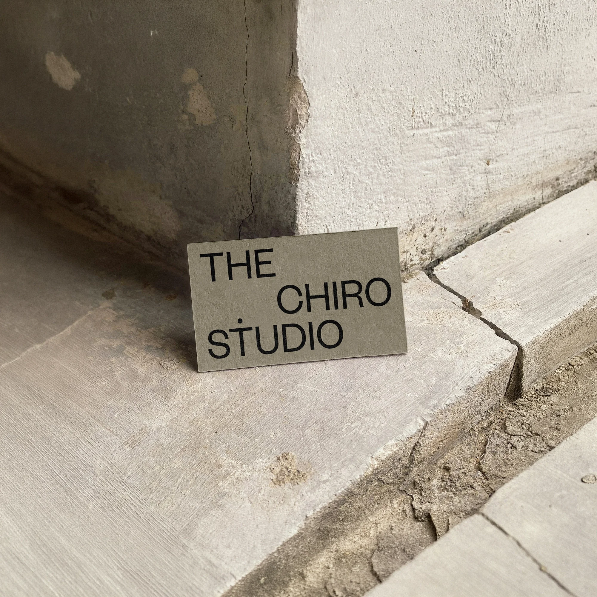 The Chiro Studio minimalist business card in sage green with bold black typography, styled on a textured stone ledge.