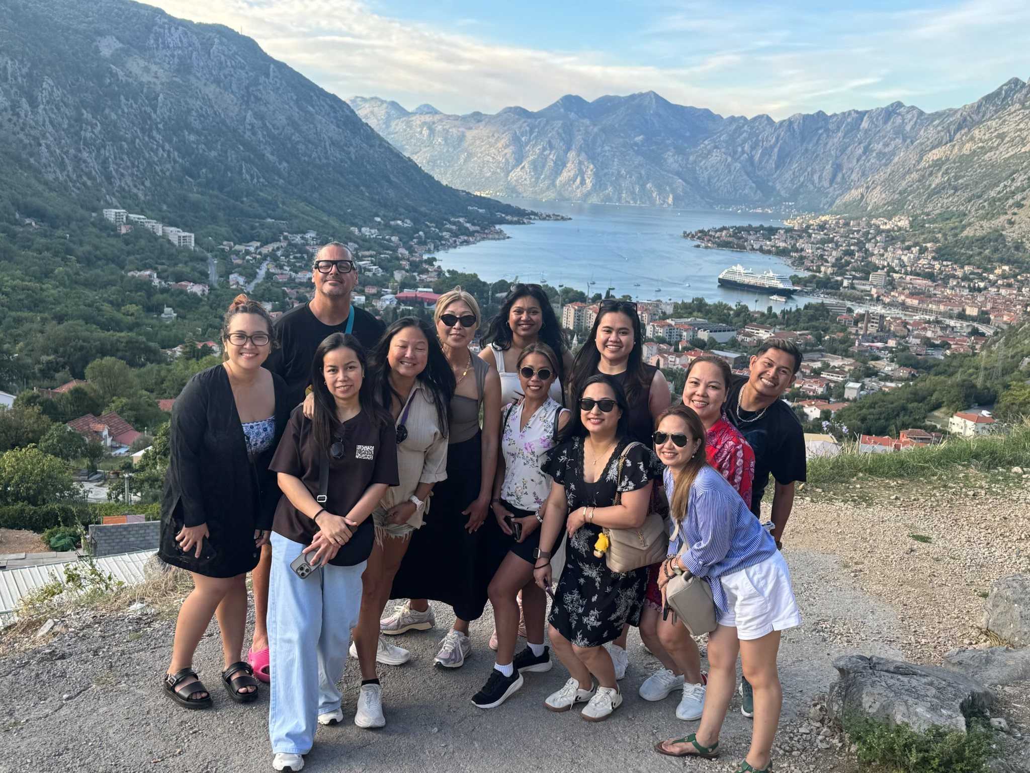 Group of eleven people standing on a hilltop with a scenic lake and mountains in the background.