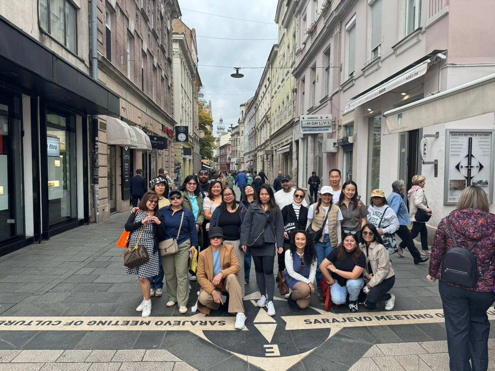 Group of people posing on a street in Sarajevo, with shops and buildings on either side.
