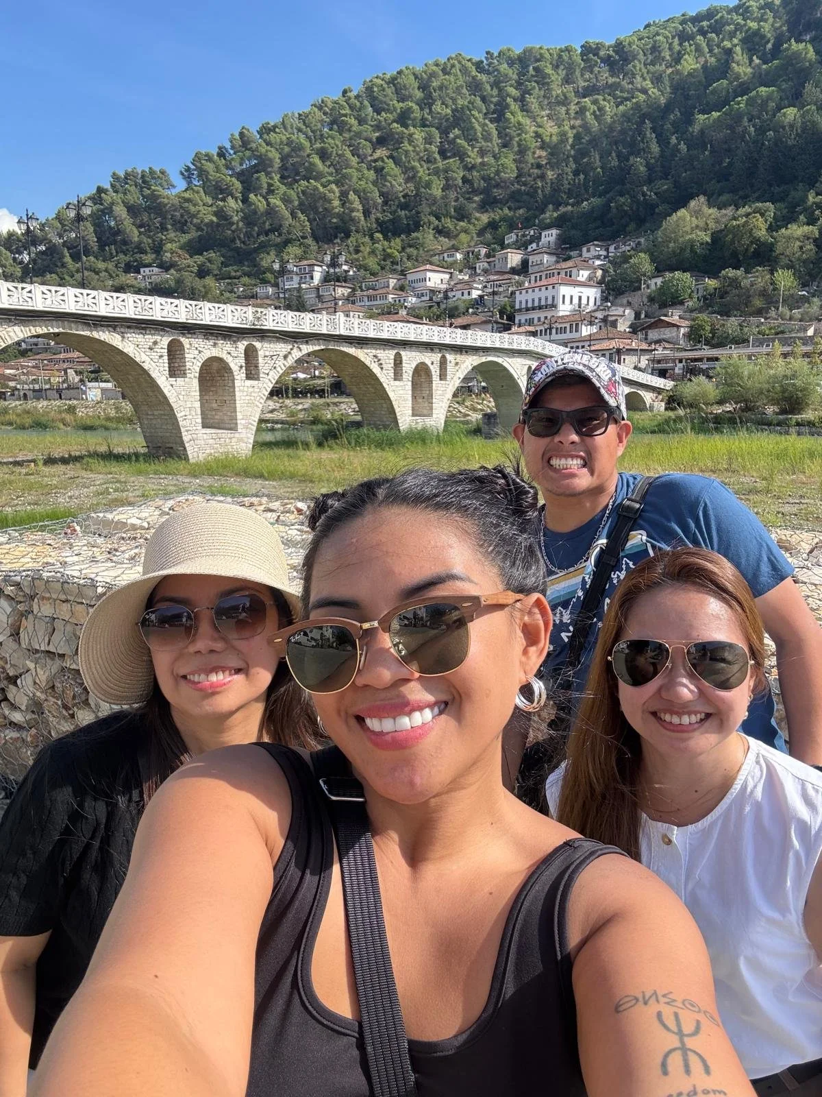 Group of five friends taking a selfie outdoors with a stone bridge and hillside town in the background in Berat, Albania
