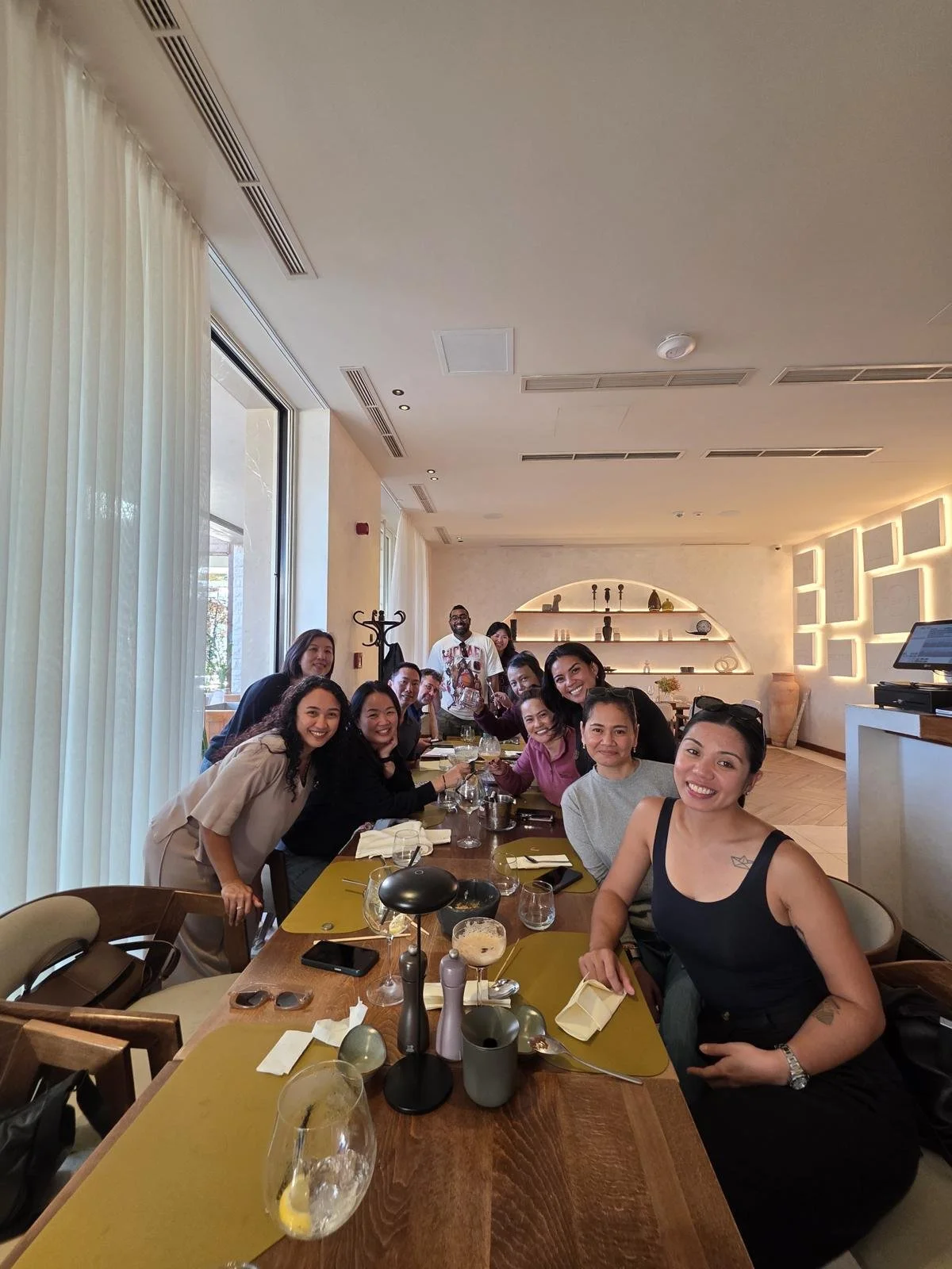 Group of people sitting at a restaurant table with drinks, smiling for the camera.
