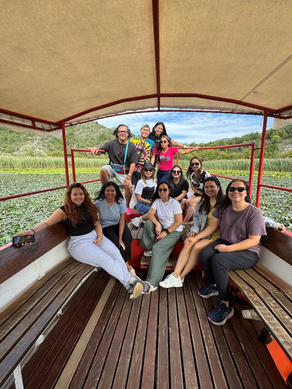 A group of people enjoying a boat ride on a scenic lake with green foliage and hills in the background in Lake Skadar, Montenegro.