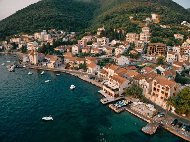 Aerial view of a coastal town with boats docked at the harbor, surrounded by hillside with houses and greenery.