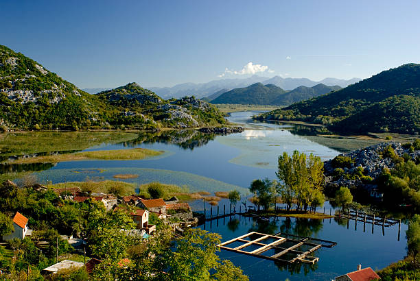 A scenic view of a river surrounded by green hills and mountains under a clear blue sky with a few clouds.