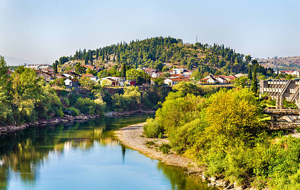 A river flowing through a lush, green landscape with houses on the hillside and trees along the water.
