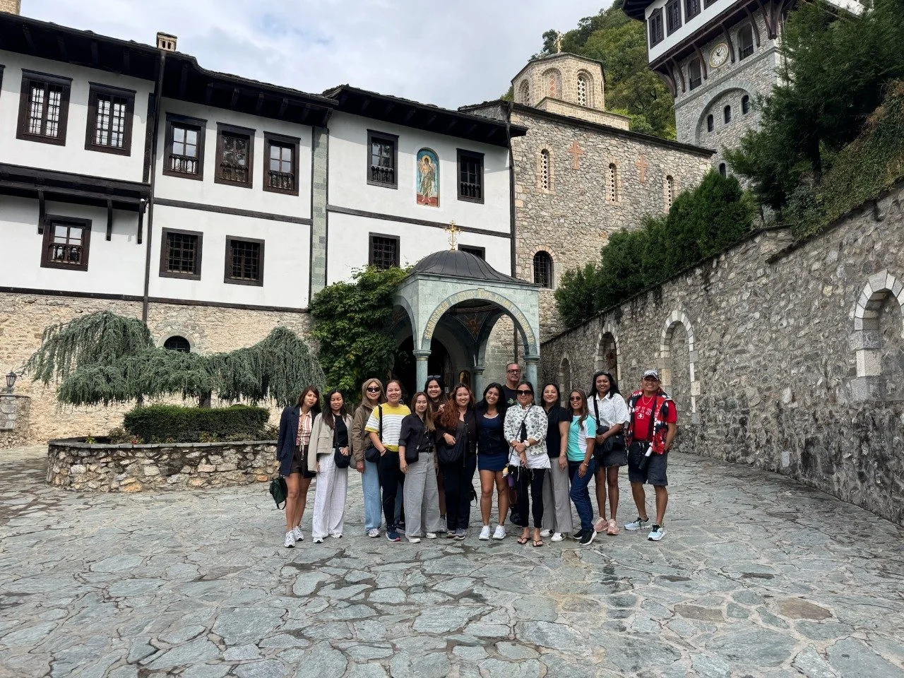 A group of tourists standing together in front of historic stone and timber buildings on a cobblestone street.