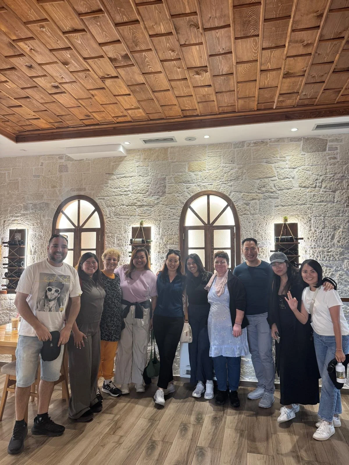 Group of nine people smiling and posing for a photo indoors, with stone walls and arched windows in the background inside the famous Eni Traditional food restaurant in Berat, Albania