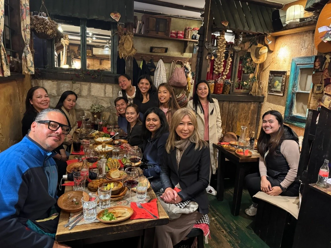 A group of people gathered around a dining table in a cozy restaurant, enjoying a meal together and smiling at the camera.