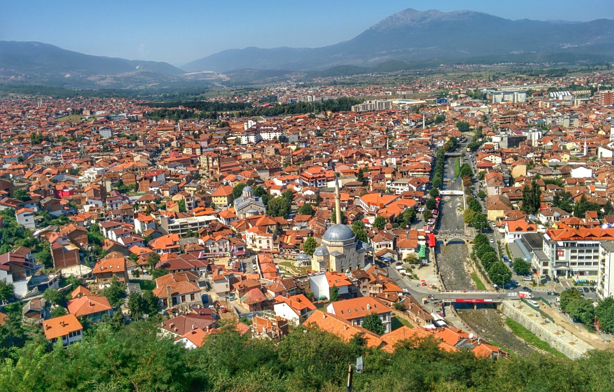 Aerial view of a city with orange rooftops, mountains in the background, and a river running through the city center.