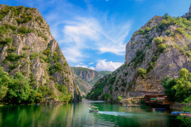 A scenic river flowing between steep, rocky mountains with green trees, under a partly cloudy sky.