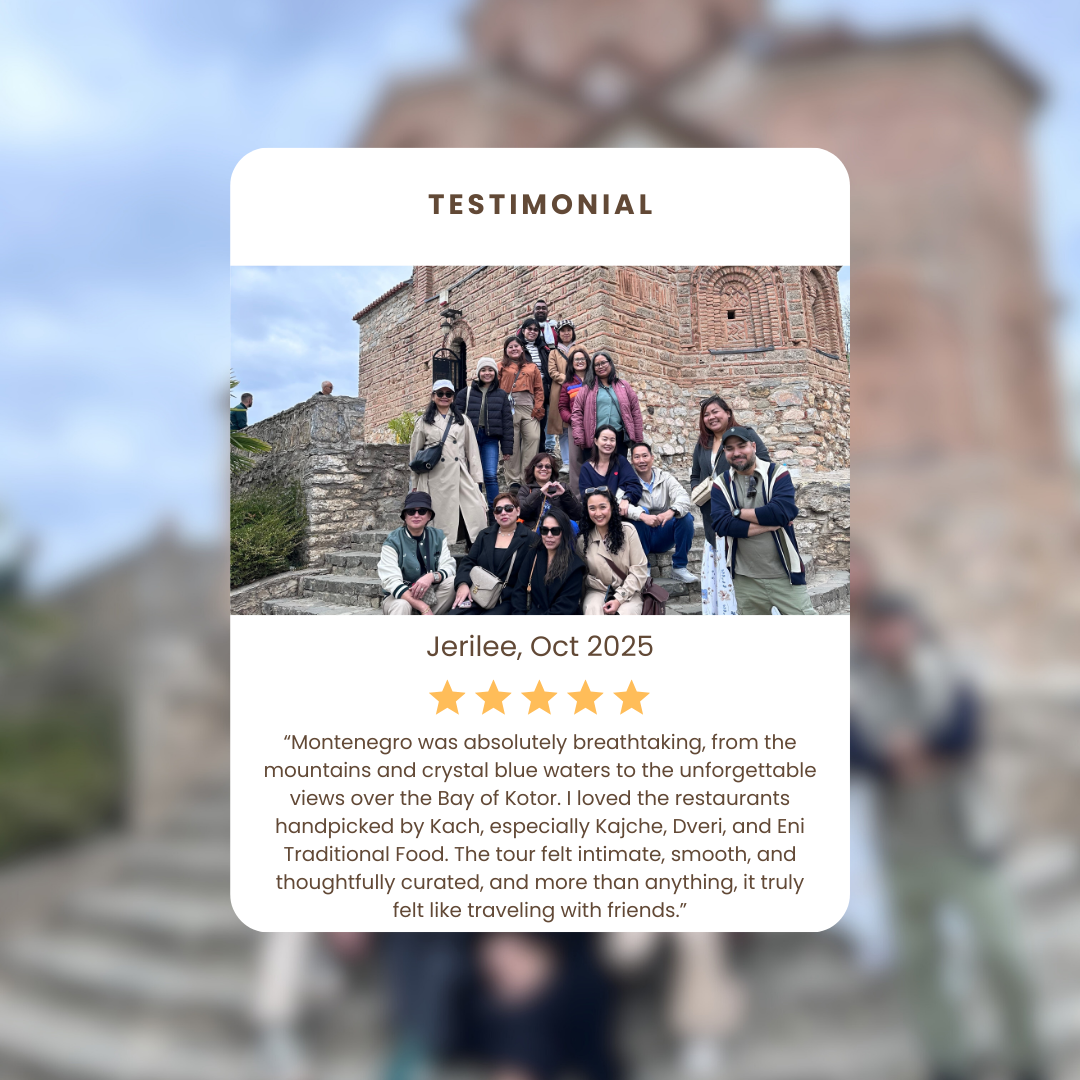 A group of people posing for a photo on the steps of a historic brick building in Montenegro, with cloudy skies in the background.