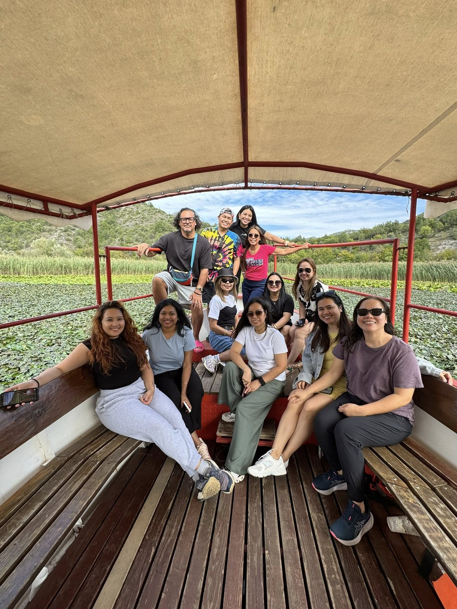 Group of people on a boat in a lake with green foliage and hills in the background.