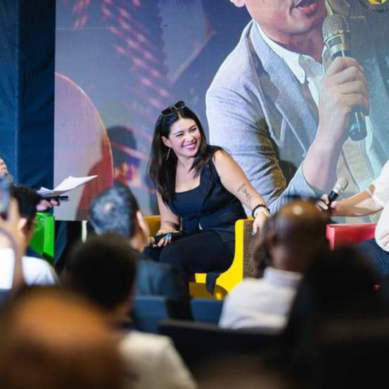 A woman smiling and sitting on a yellow chair during a panel discussion at a conference or event.