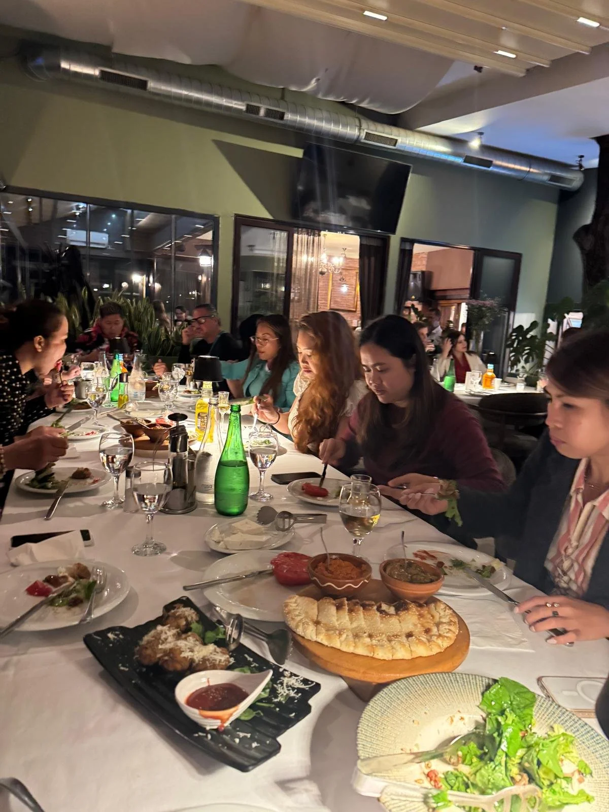 A group of people eating dinner at a restaurant with a variety of dishes on the table, including bread, salads, and cooked items.