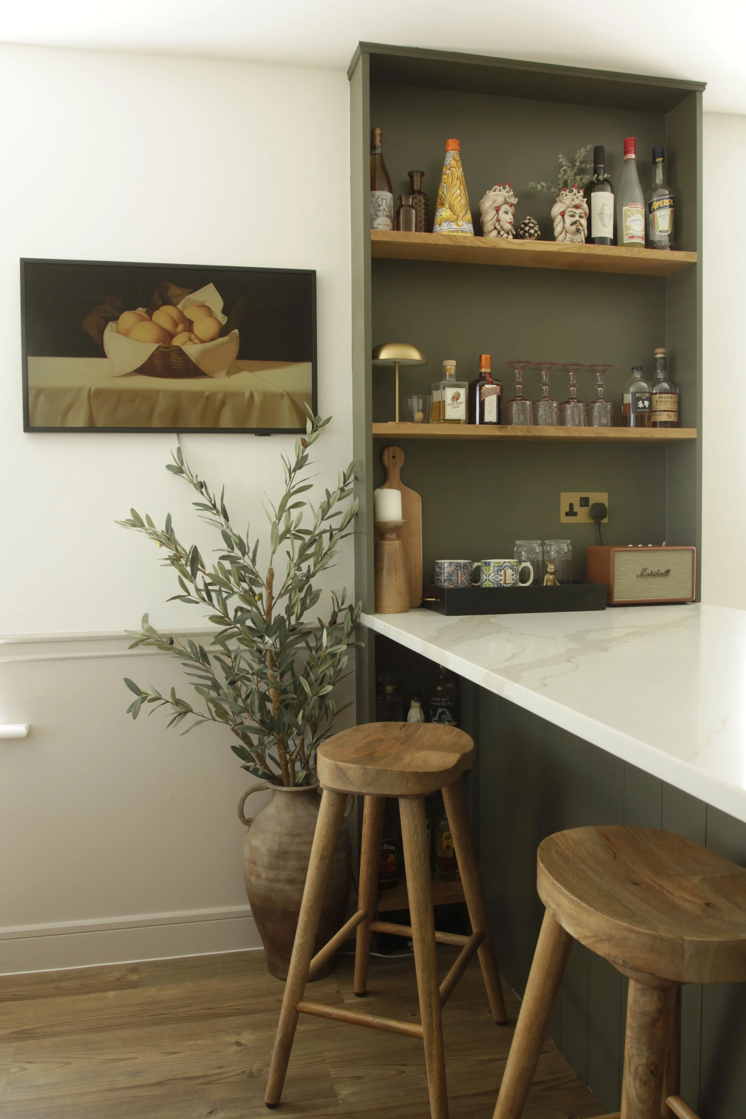 Built-in home bar with open oak shelving, quartz breakfast bar and dark olive green cabinetry.