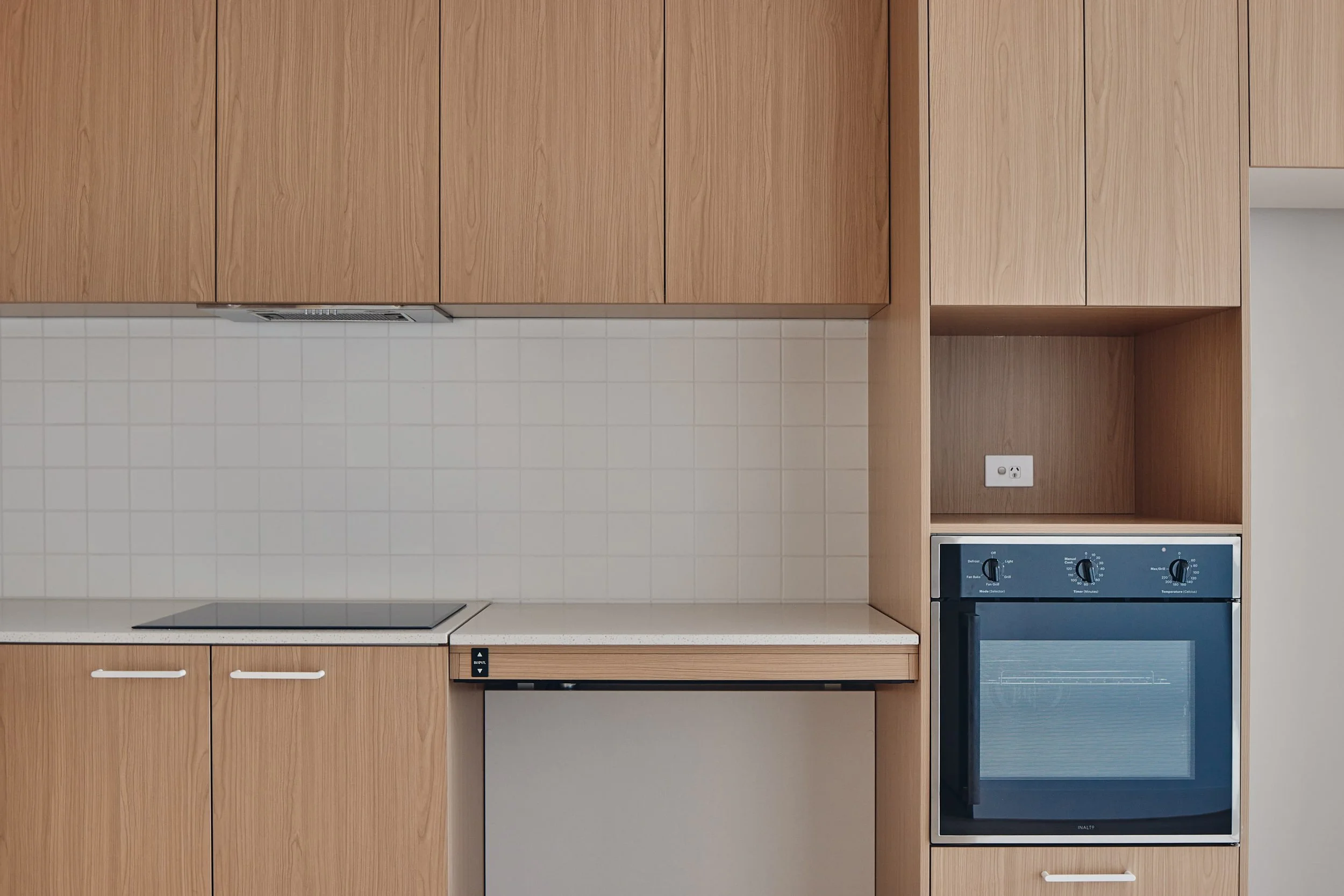 Modern kitchen with wood cabinets, a stovetop, oven, and white tile backsplash. Minimalist and clean design.