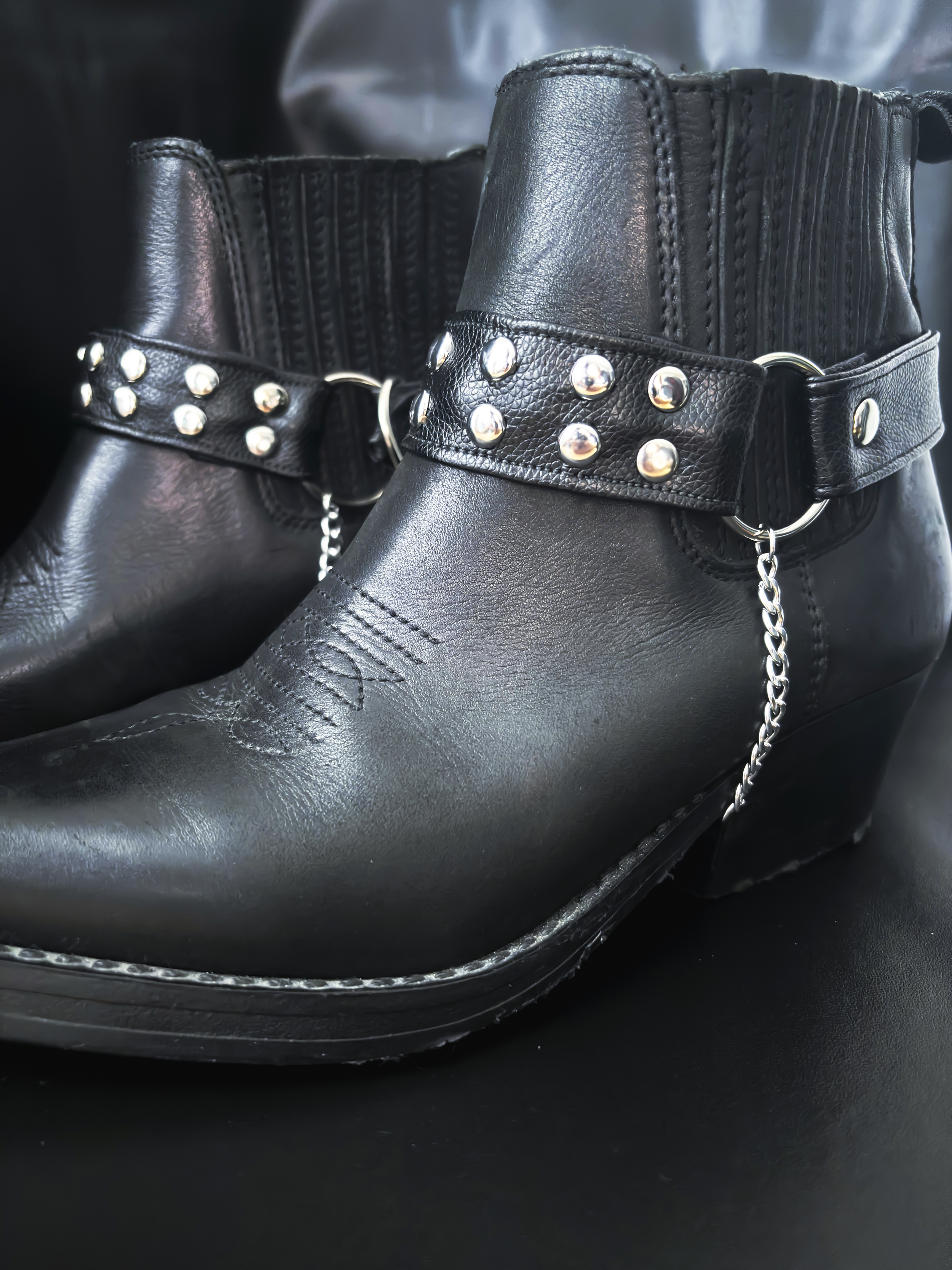 Close-up of Hellion boot straps in black vegan leather, detailed with polished round studs and a detachable chain. Handmade in Helsinki.