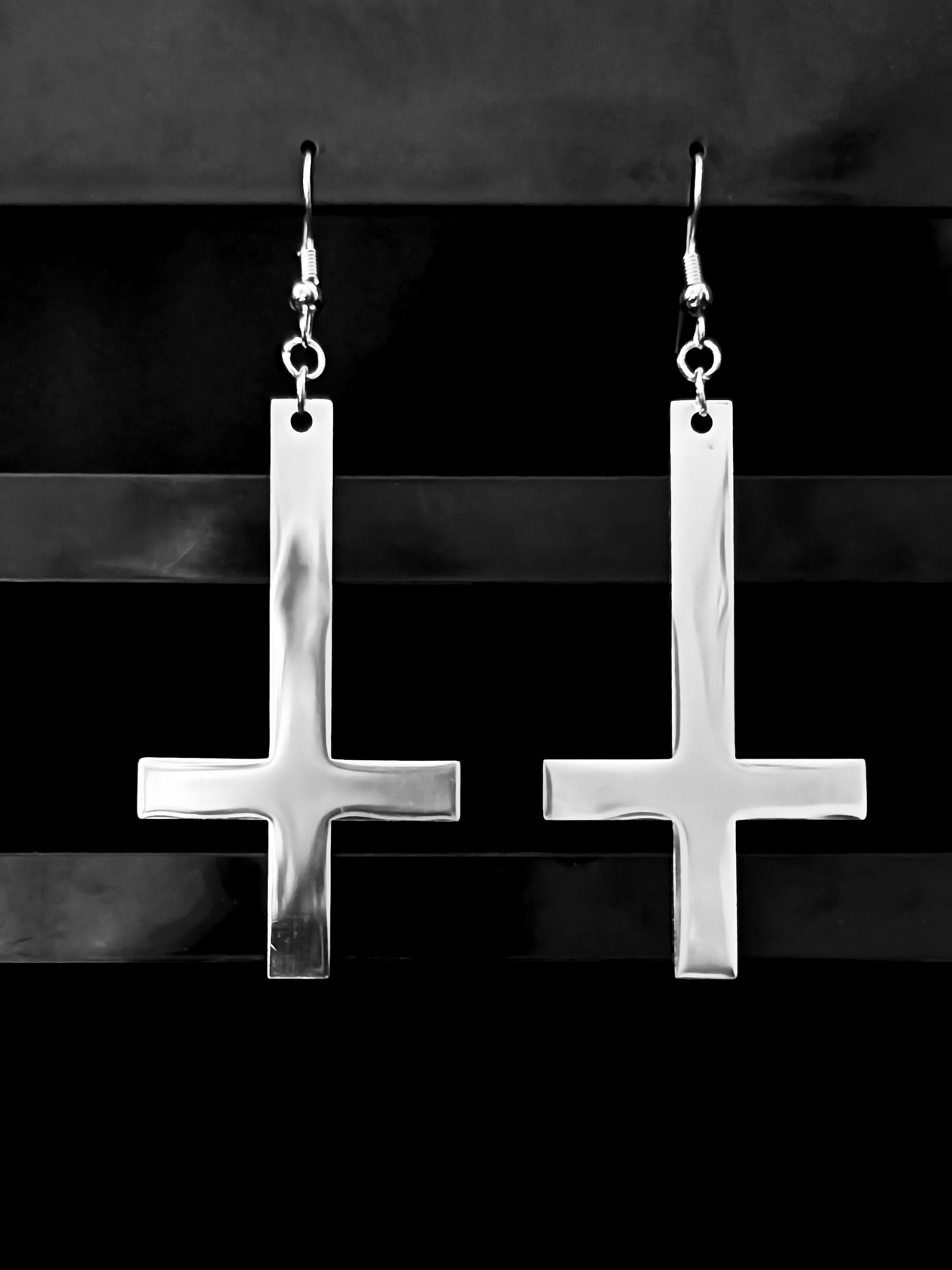 Close-up of Obsidian Inversion’s 5 cm inverted cross pendant in gleaming stainless steel, suspended from a hoop.