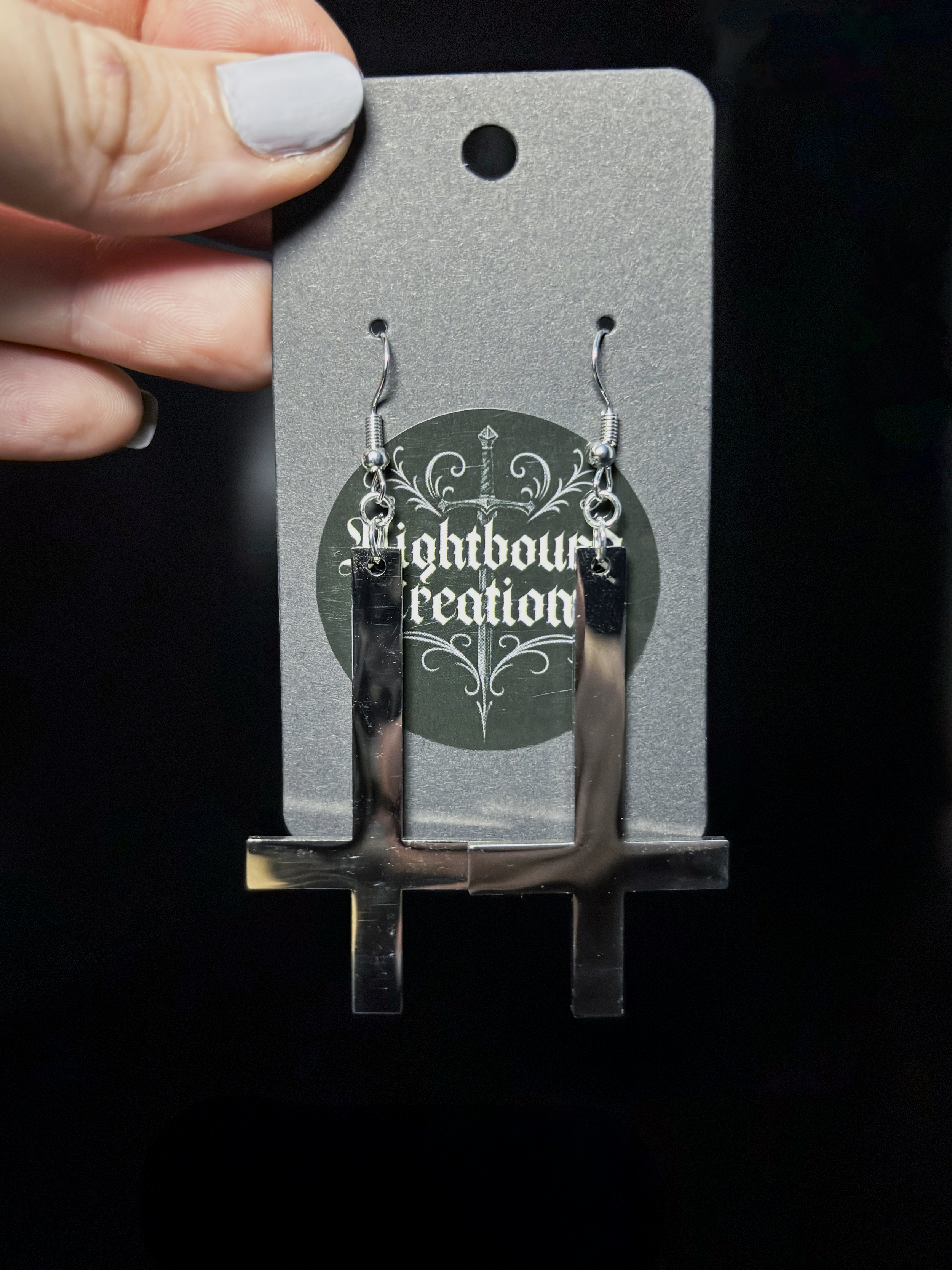 Obsidian Inversion earrings arranged on charcoal fabric, the reversed crosses casting subtle shadows.