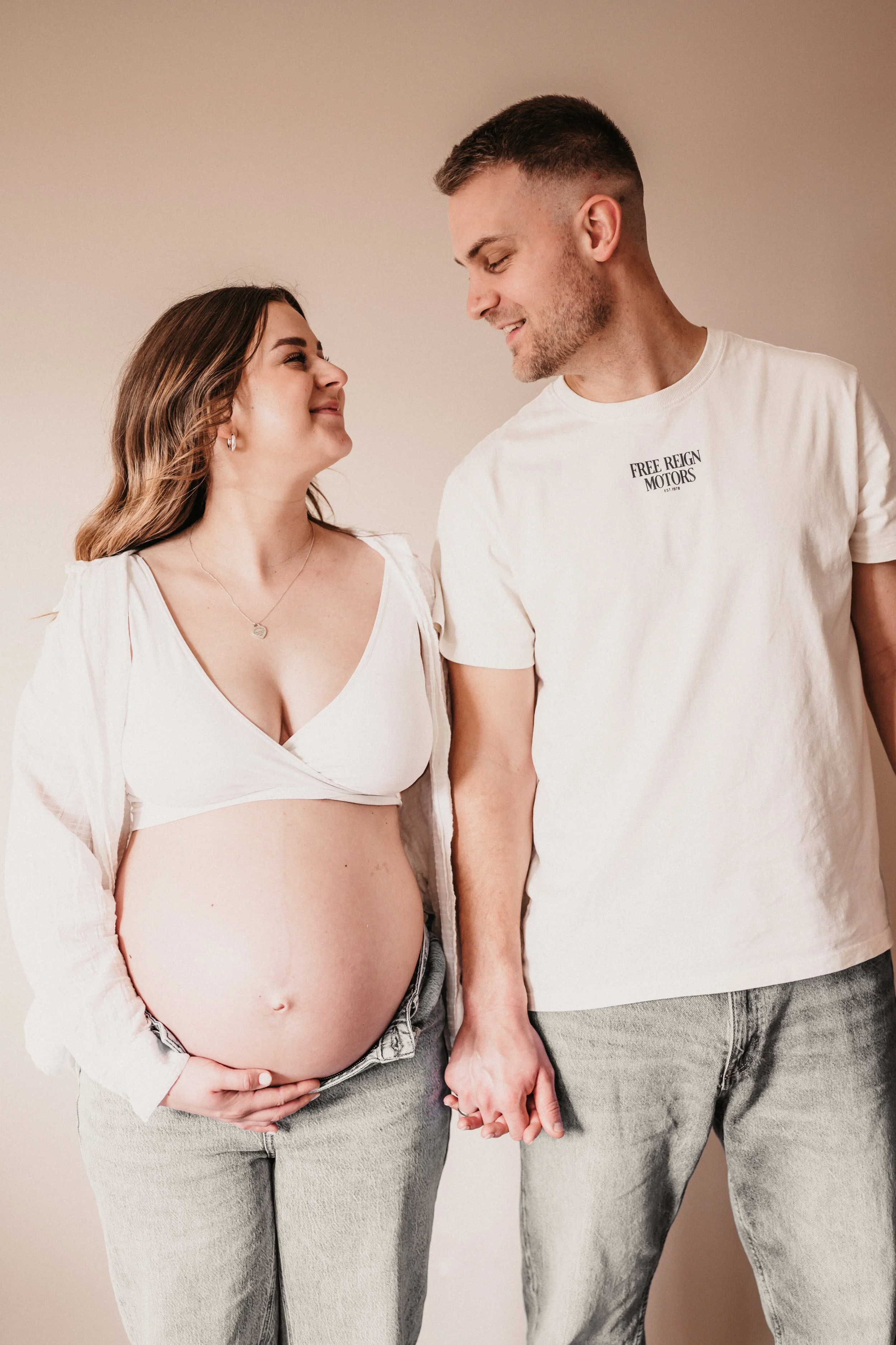Ein schwangeres Paar hält Händchen und schaut sich liebevoll an, die Frau zeigt ihren Babybauch.