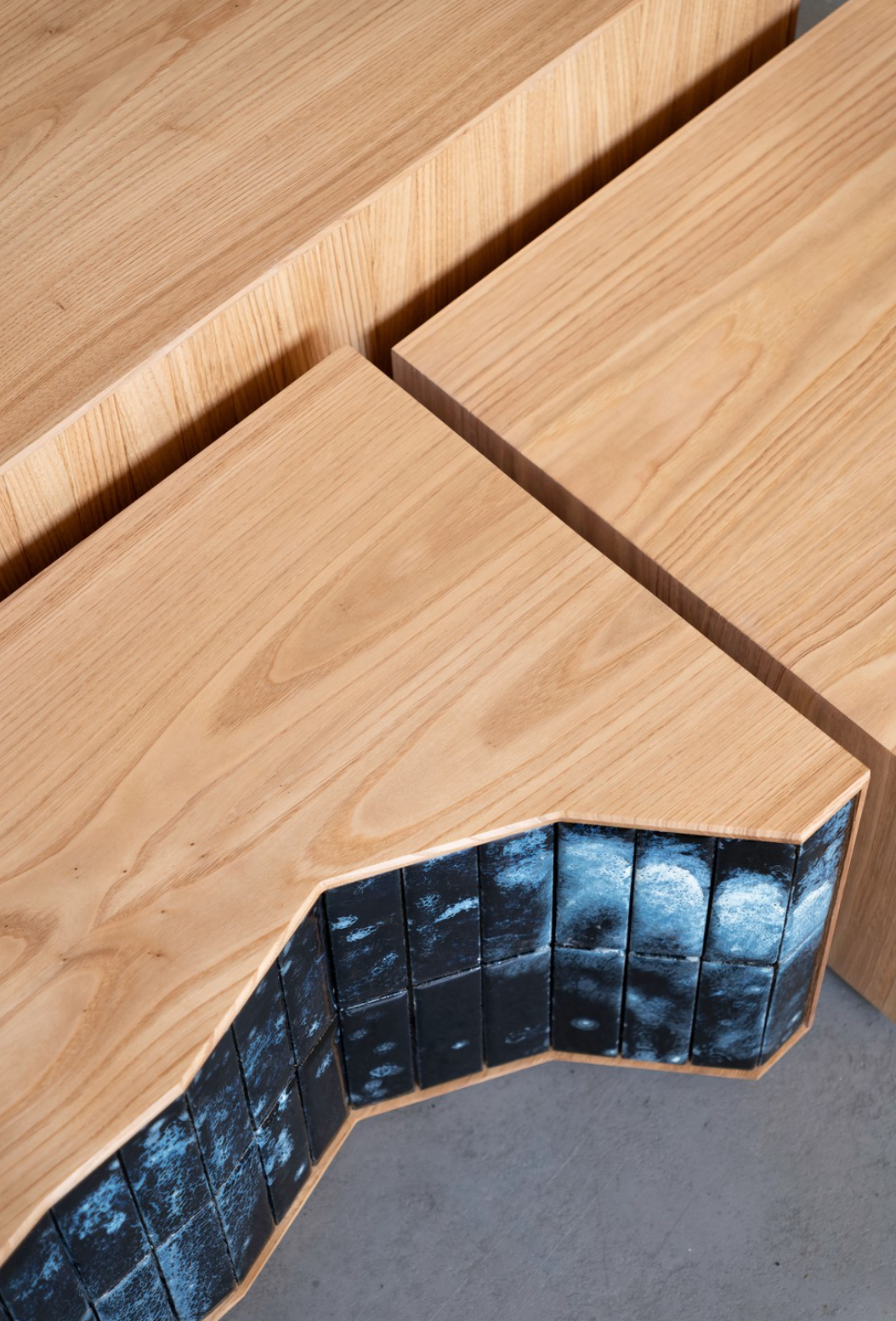 Detalhe de três mesas de café em madeira com acabamento natural com uma face coberta de azulejos decorativos em tons de azul.