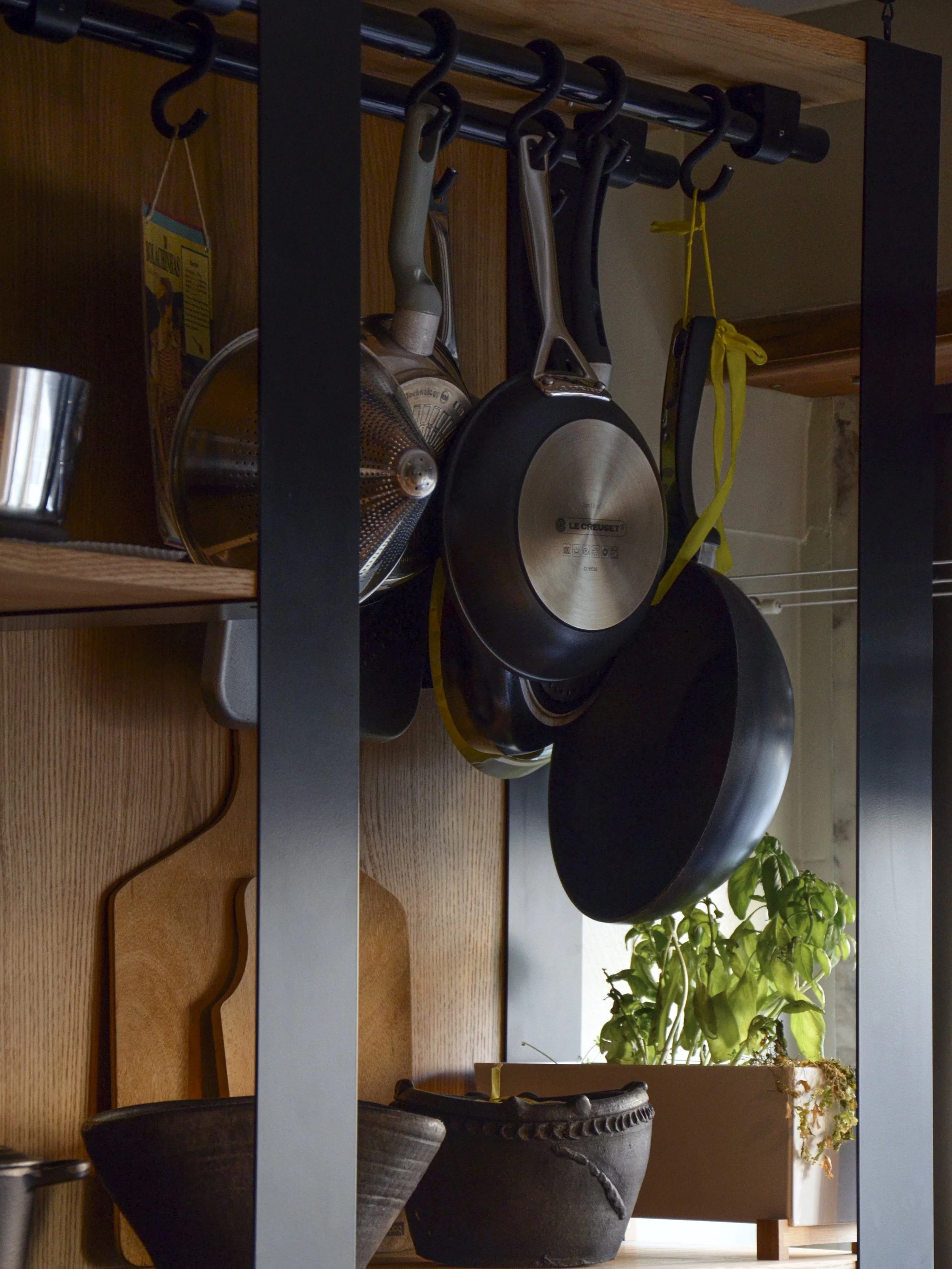 Armário aberto folheado a carvalho americano, com barras em ferro termolacado para arrumação flexível de tachos e utensílios de grande dimensão.