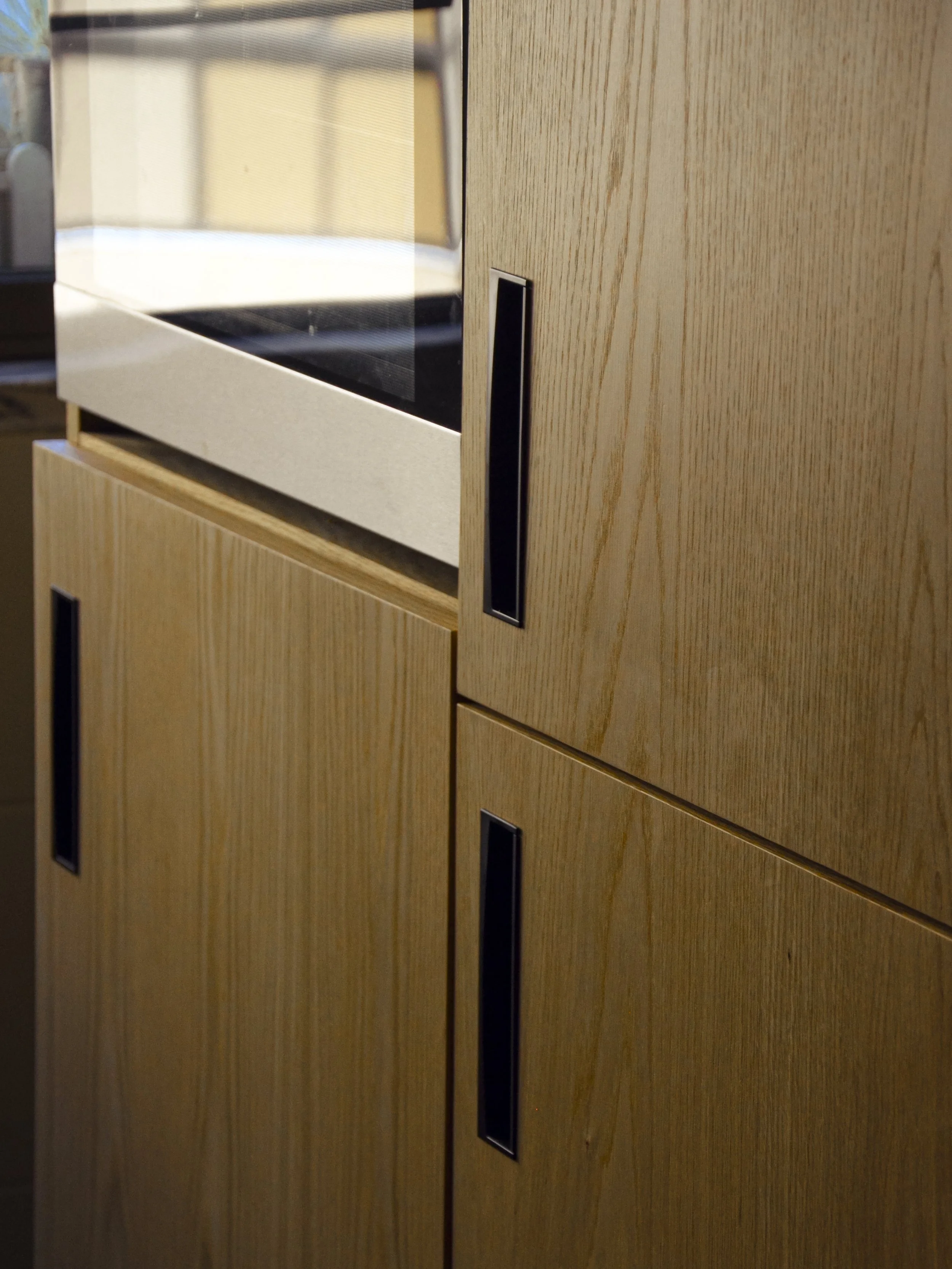 Armários com eletrodomésticos encastrados, folheados a carvalho americano, com elementos em ferro termolacado.