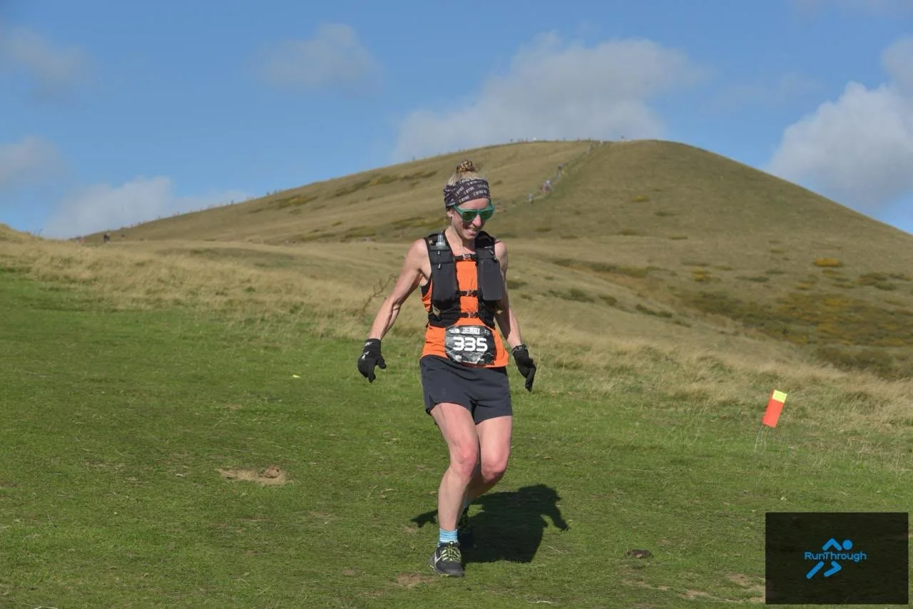 Claire from Beyond Running running downhill on the Ladybower Trail Half Marathon, with a steep Peak District hill behind