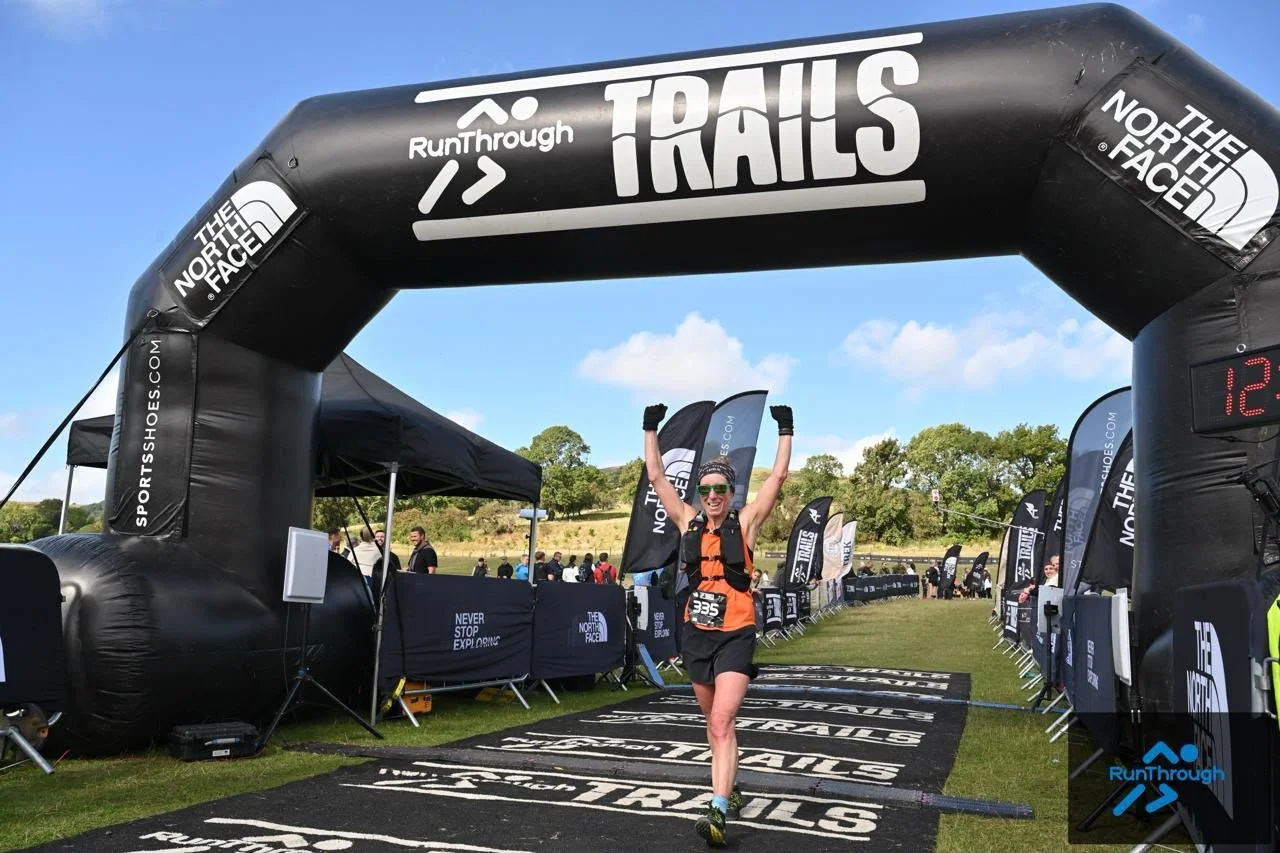 Claire from Beyond Running crossing the RunThrough Trails finish line at the Ladybower Trail Half Marathon, arms raised