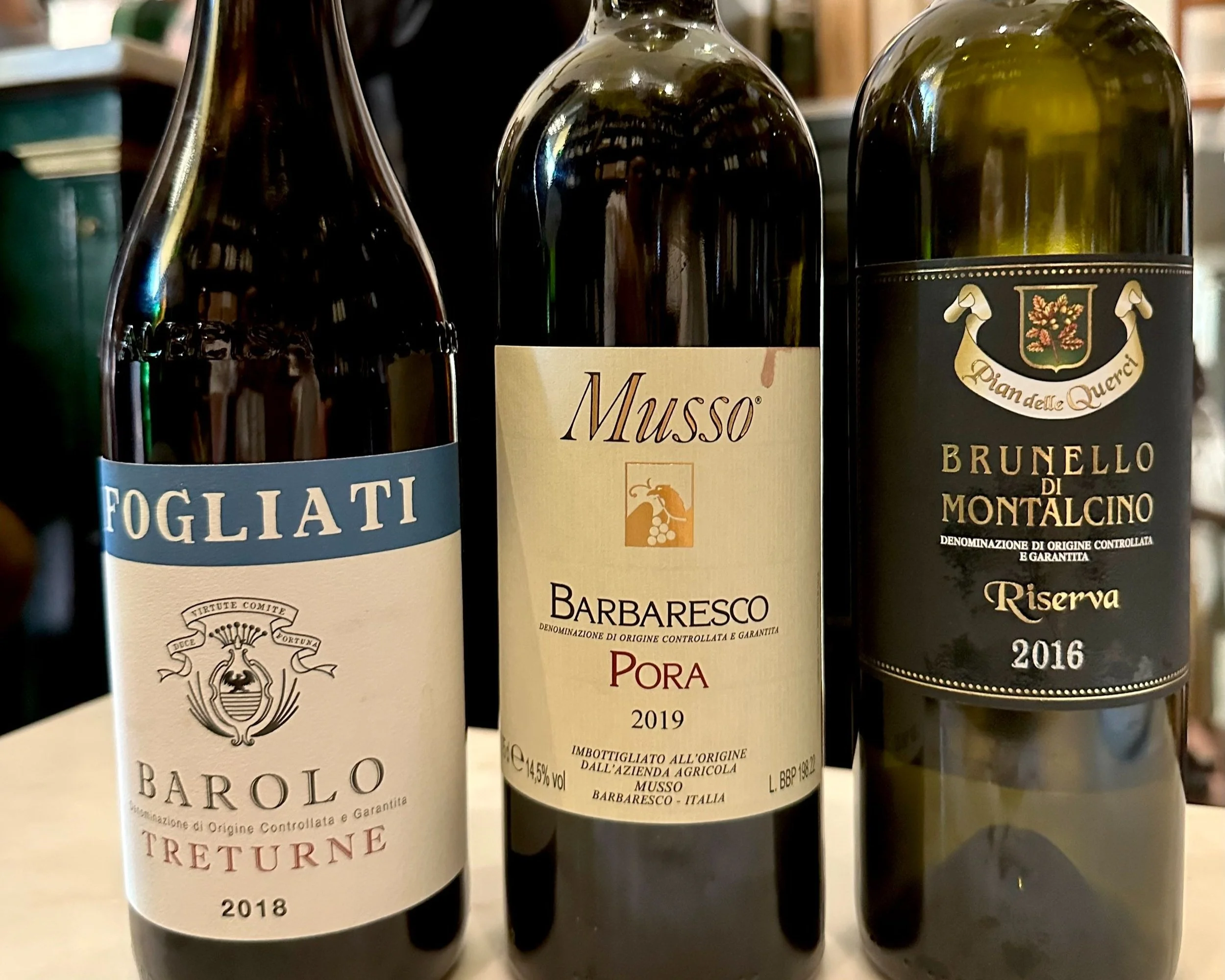 Three bottles of Italian red wine placed on a table. From left to right: a 2018 Barolo Treturne, a 2019 Barbaresco Pora, and a 2016 Brunello di Montalcino Riserva.