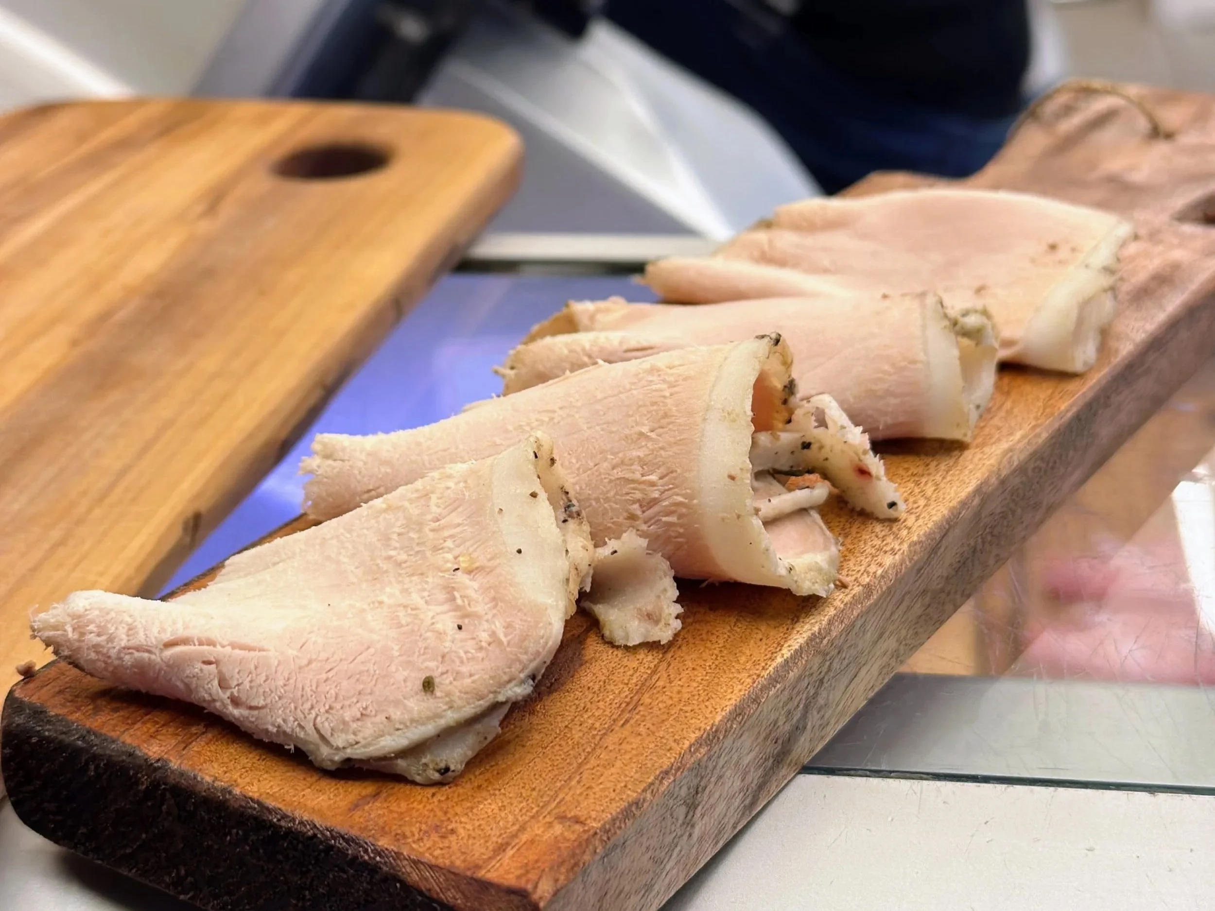 Slices of cooked chicken breast on a wooden serving board.