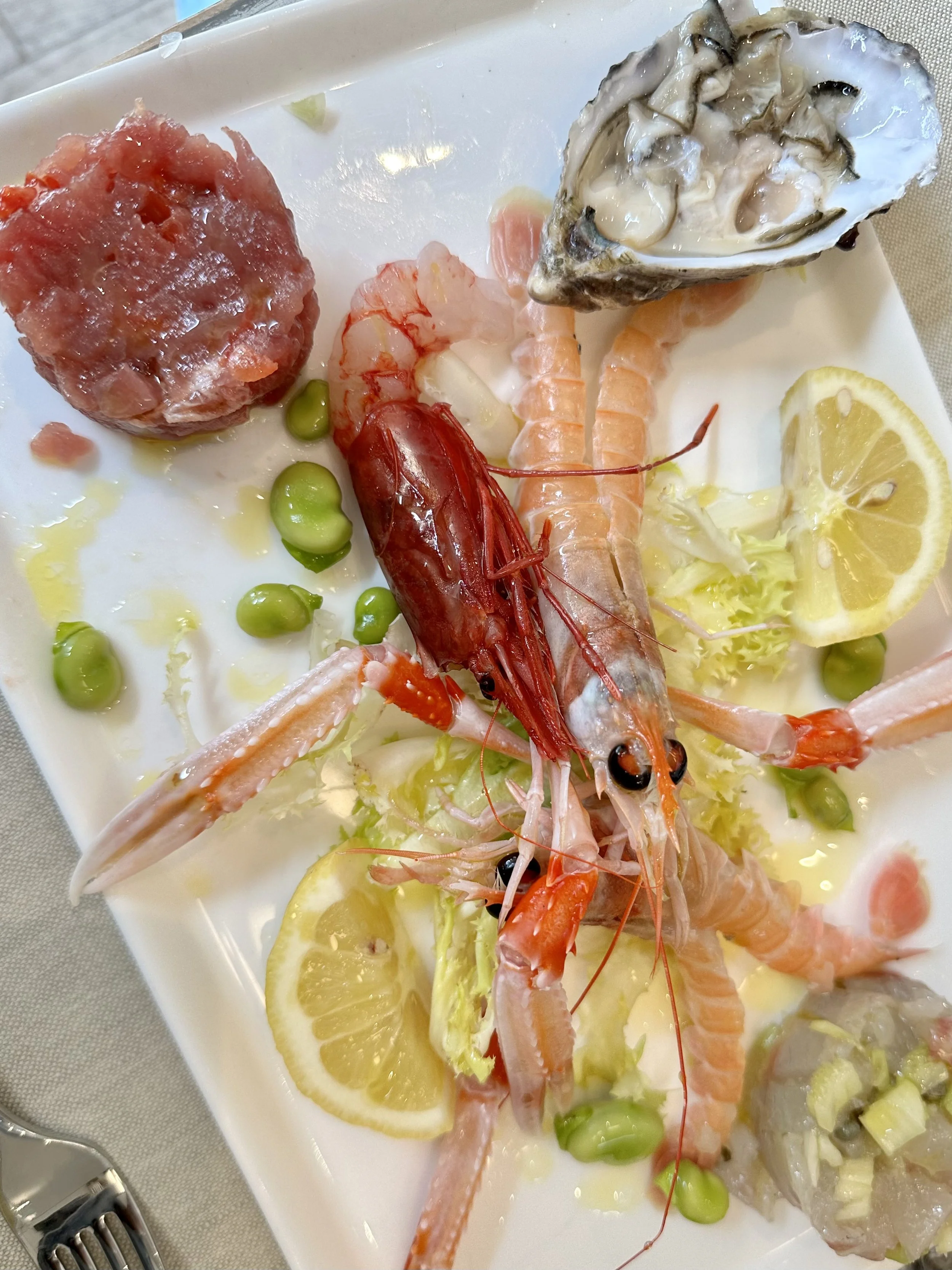 Seafood platter with shrimp, oysters, lemon wedges, green peas, and a seafood mixture, served on a white plate.