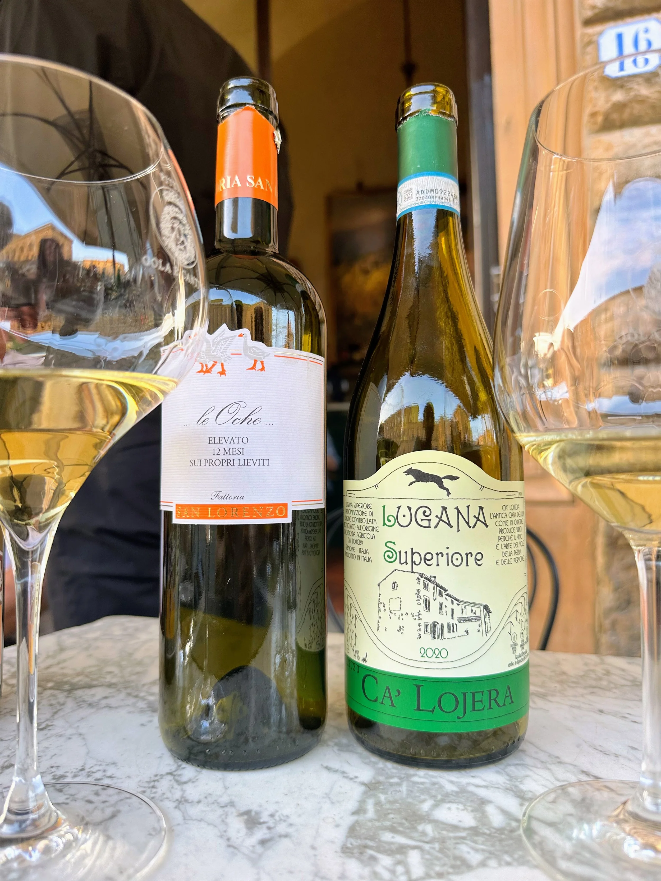 Two bottles of white wine with two glasses of white wine on a marble table.