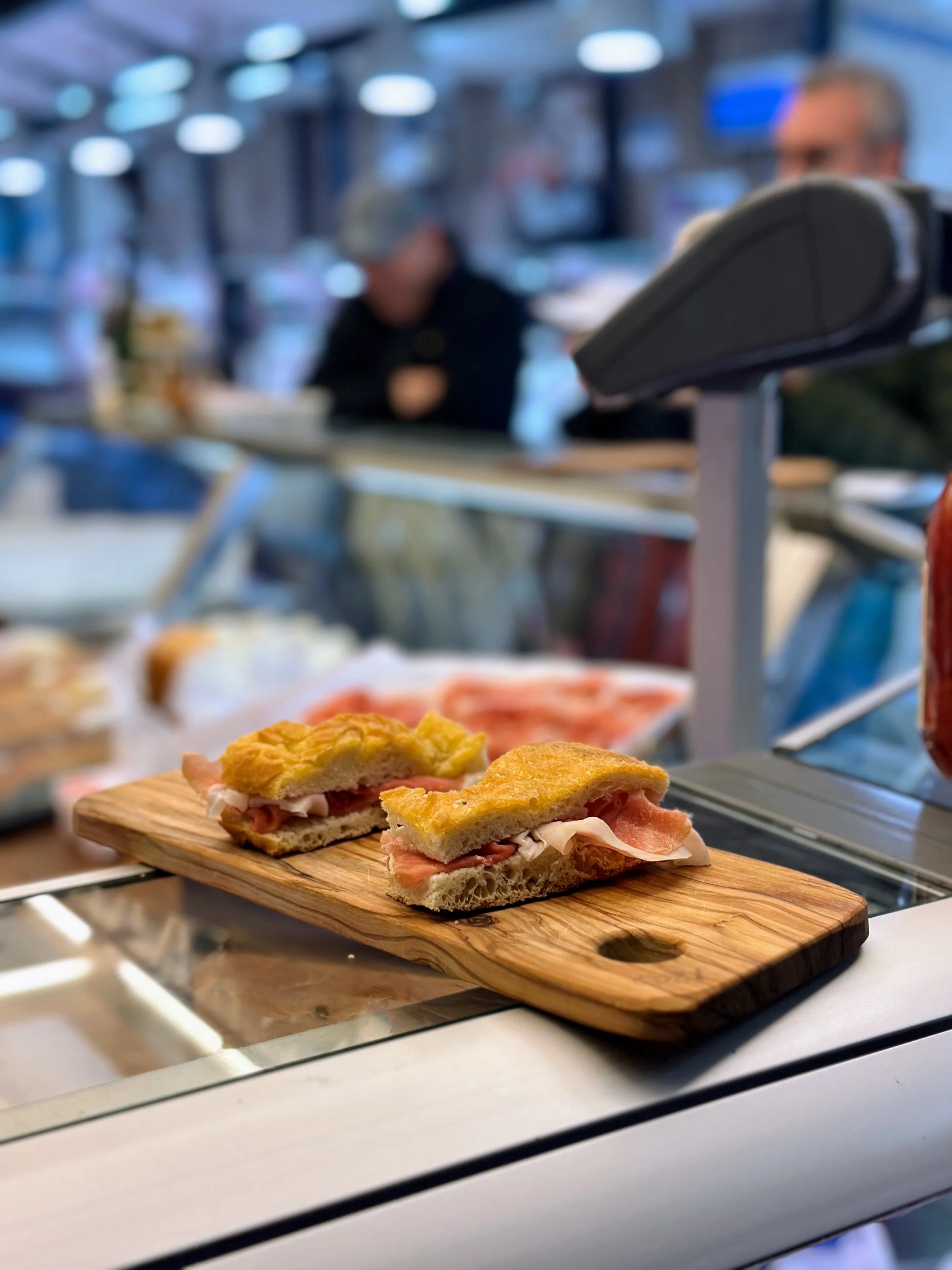 Close-up of a sandwich with ham and turkey on a wooden serving board in a deli or cafe setting.