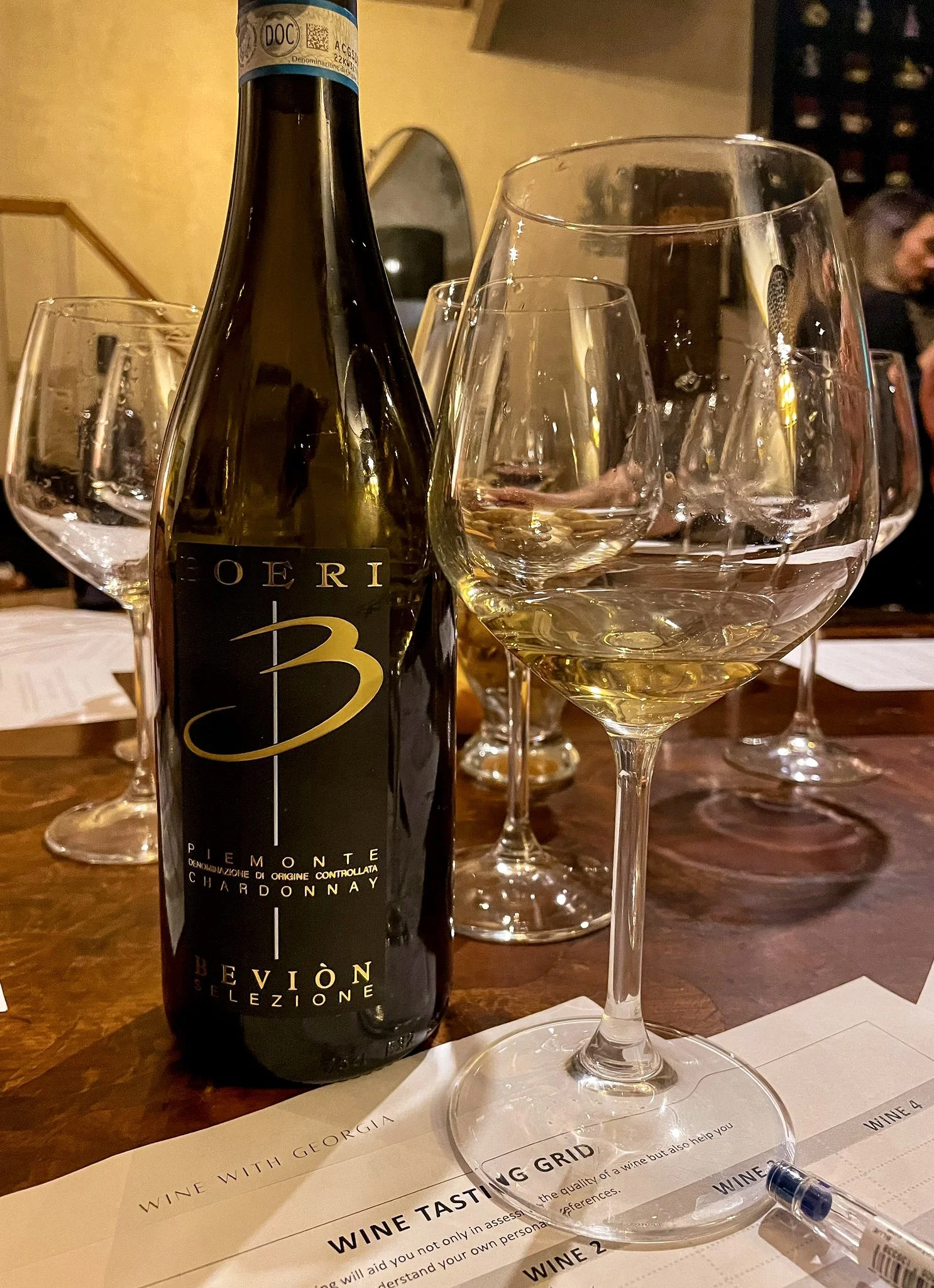 A bottle of white wine alongside several wine glasses filled with white wine on a wooden table in a restaurant setting.