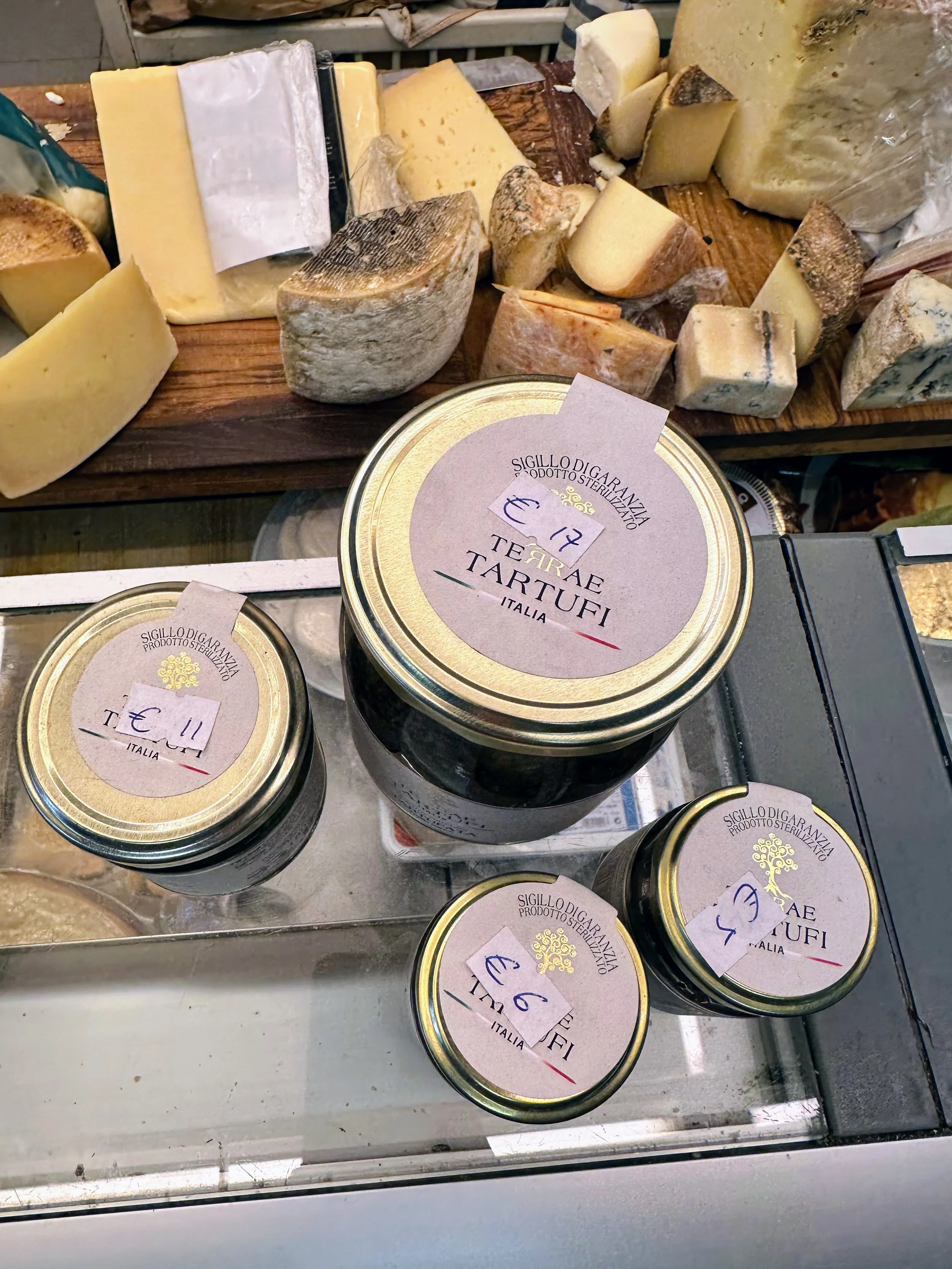 Various packaged Italian cheese jars with a wooden cheese board in the background displaying different types of cheese.