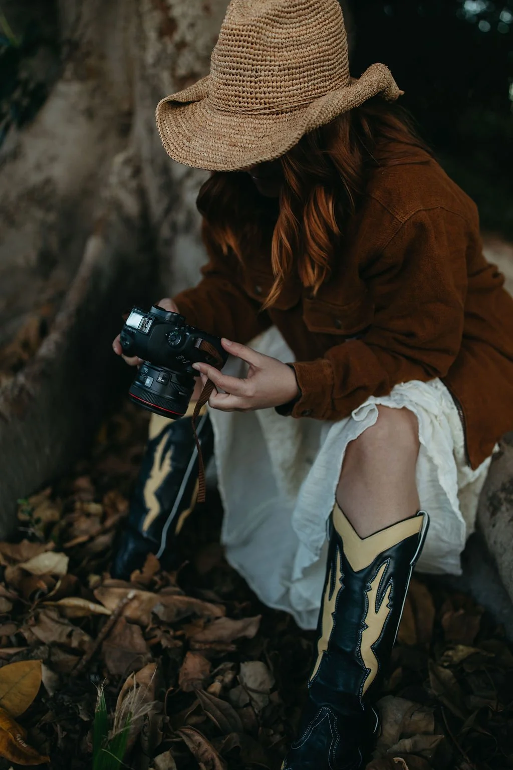 Jade Jones sitting beneath a large tree, holding her camera and looking at the screen.