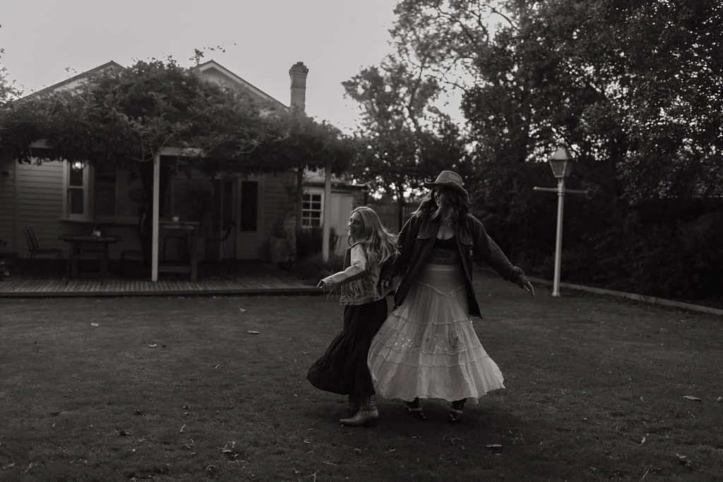 Black and white photograph of Jade and her daughter twirling together in a backyard, smiling.