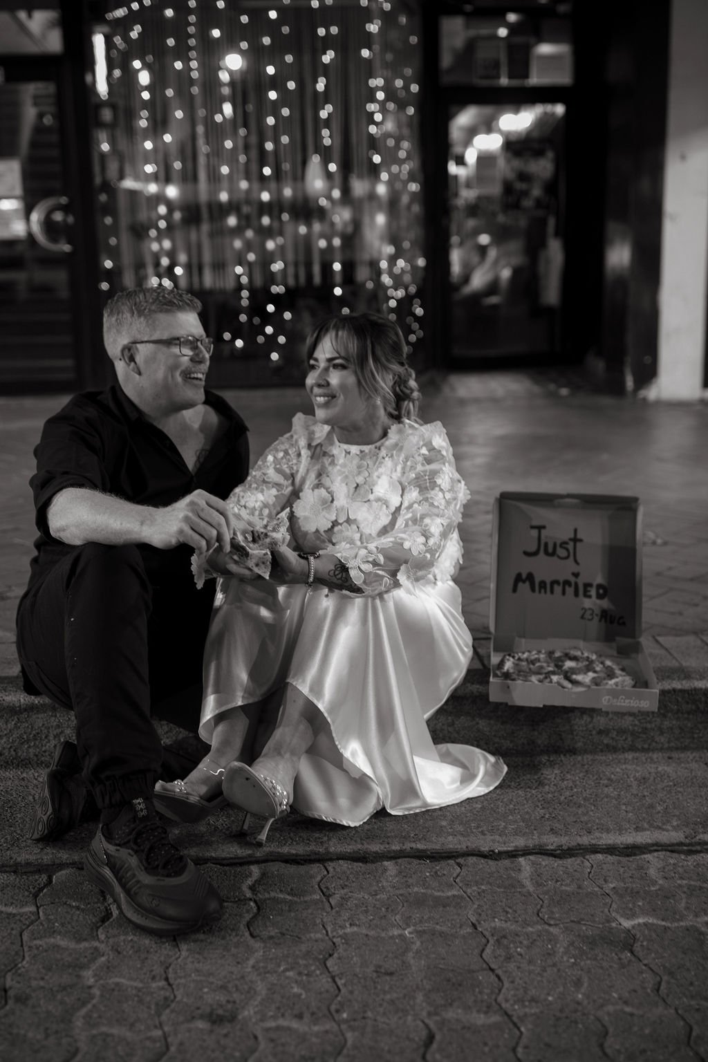 Newlyweds sitting on the stairs outside their wedding venue, enjoying pizza with "Just Married" written on the box, captured during a surprise 40th birthday wedding by Jade Jones Photography.