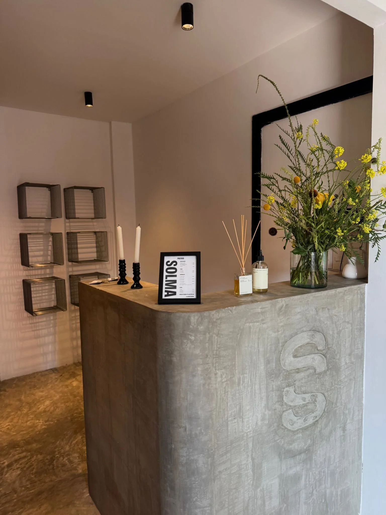 Mostrador de recepción de hotel con flores en un florero, candeleros y un cartel de precios.