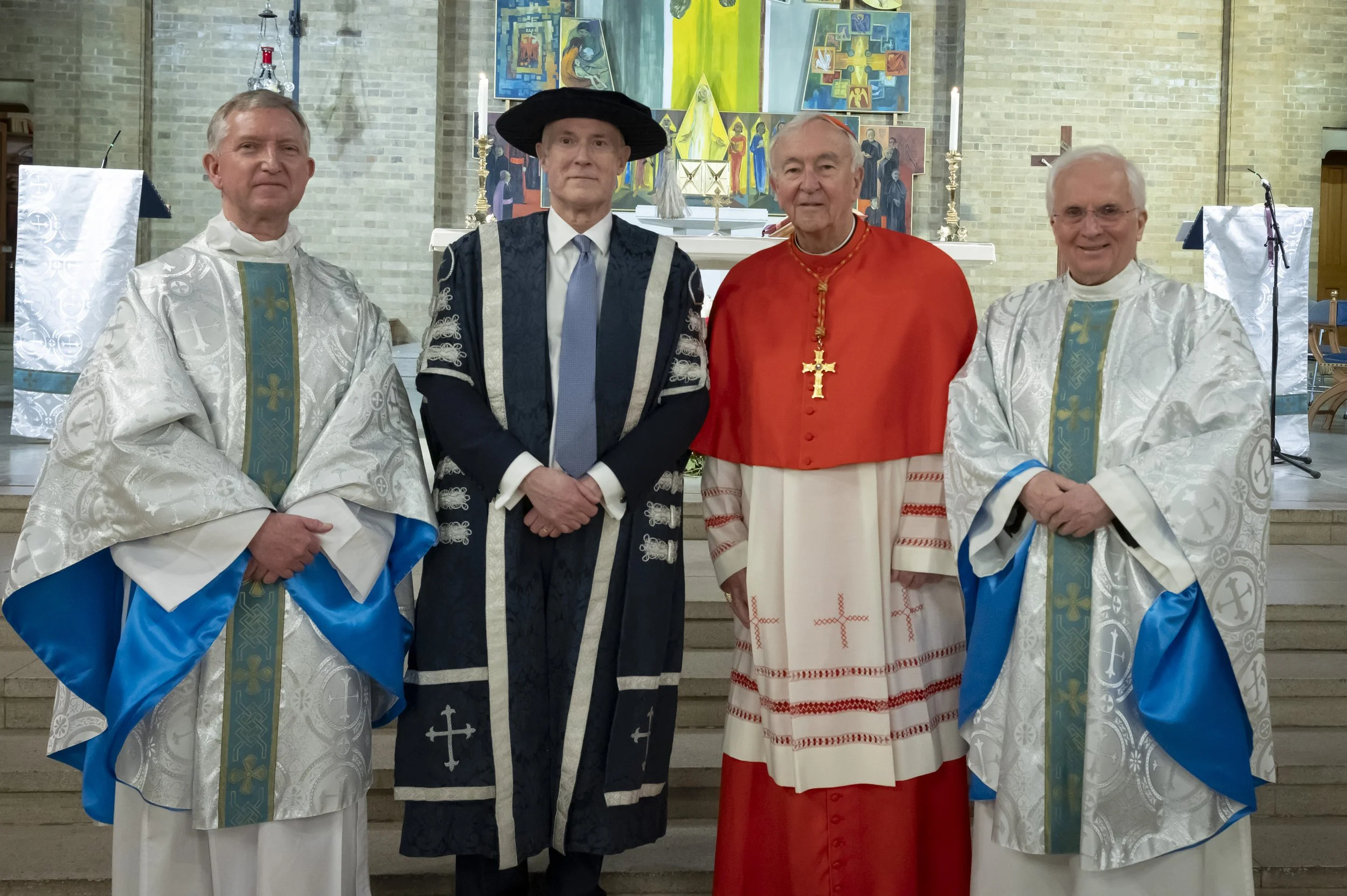 Three clergymen and St Mary's University Vice Chancellor standing in front of the alter in the Chapel, two in White Robes, one in a Red Robe and one wearing black garments and a black hat